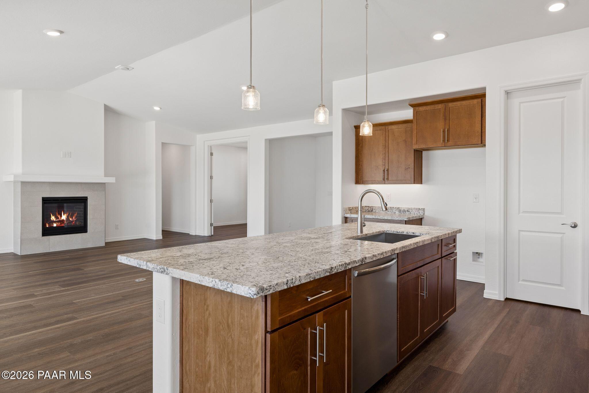 Modern open-concept kitchen featuring granite island, stainless sink, shaker cabinets, pendant lights, and cozy fireplace in Davidson Homes The Monarch A, Prescott AZ