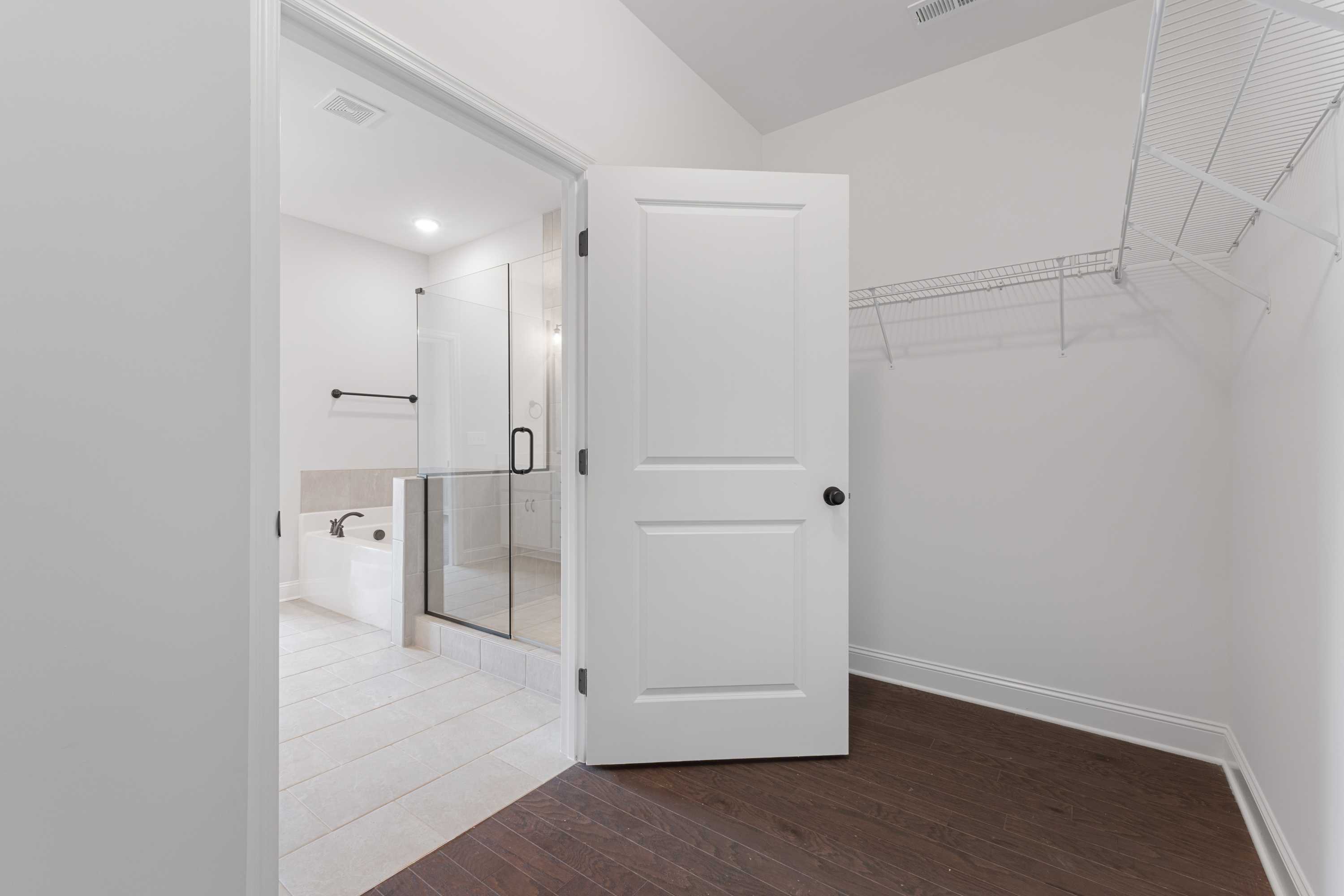 Open walk-in closet in The Copeland master suite with door ajar to modern bathroom, frameless glass shower, white tile floor