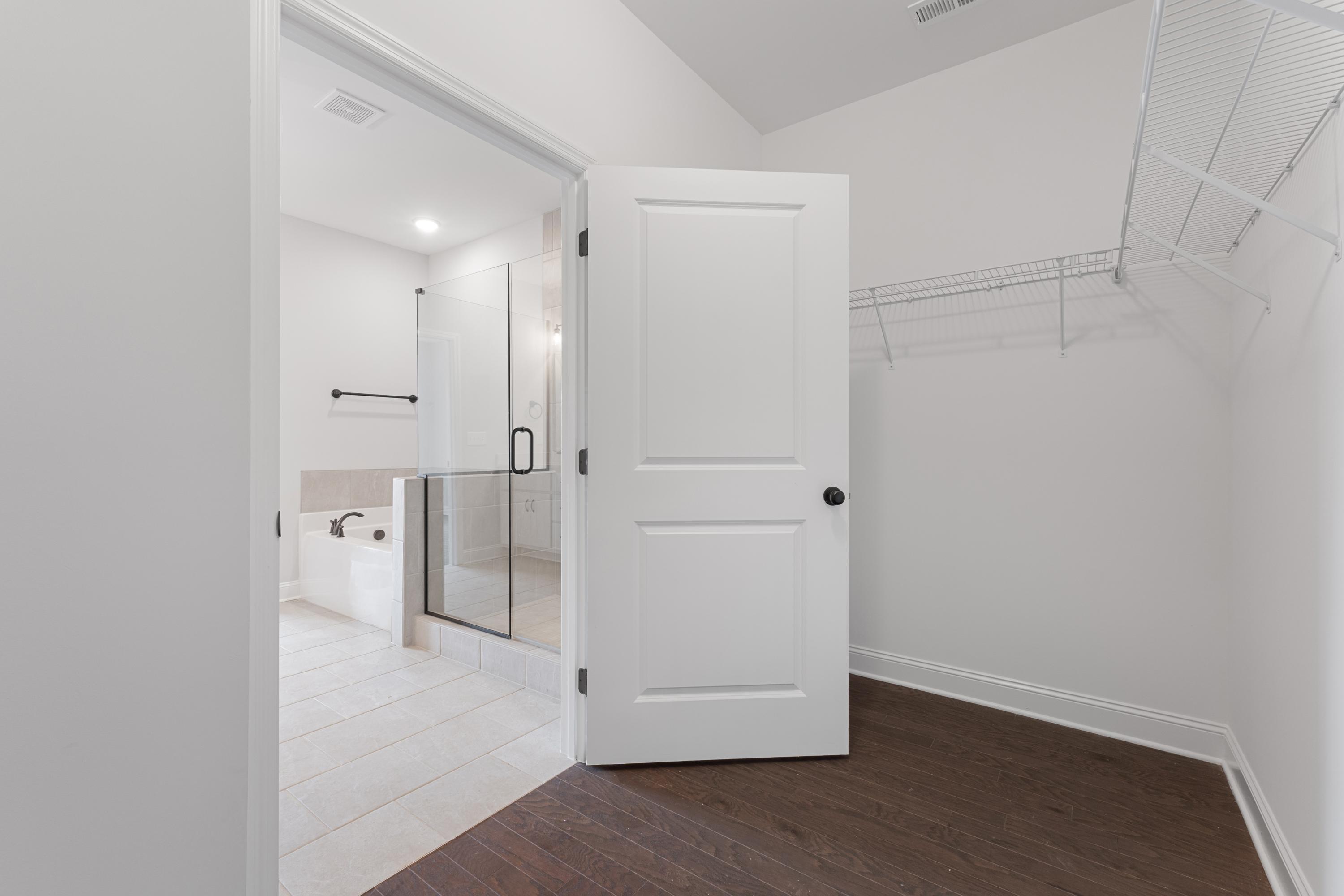 Spacious walk-in closet with wire shelving opening to modern en-suite bathroom featuring frameless glass shower in The Copeland master suite