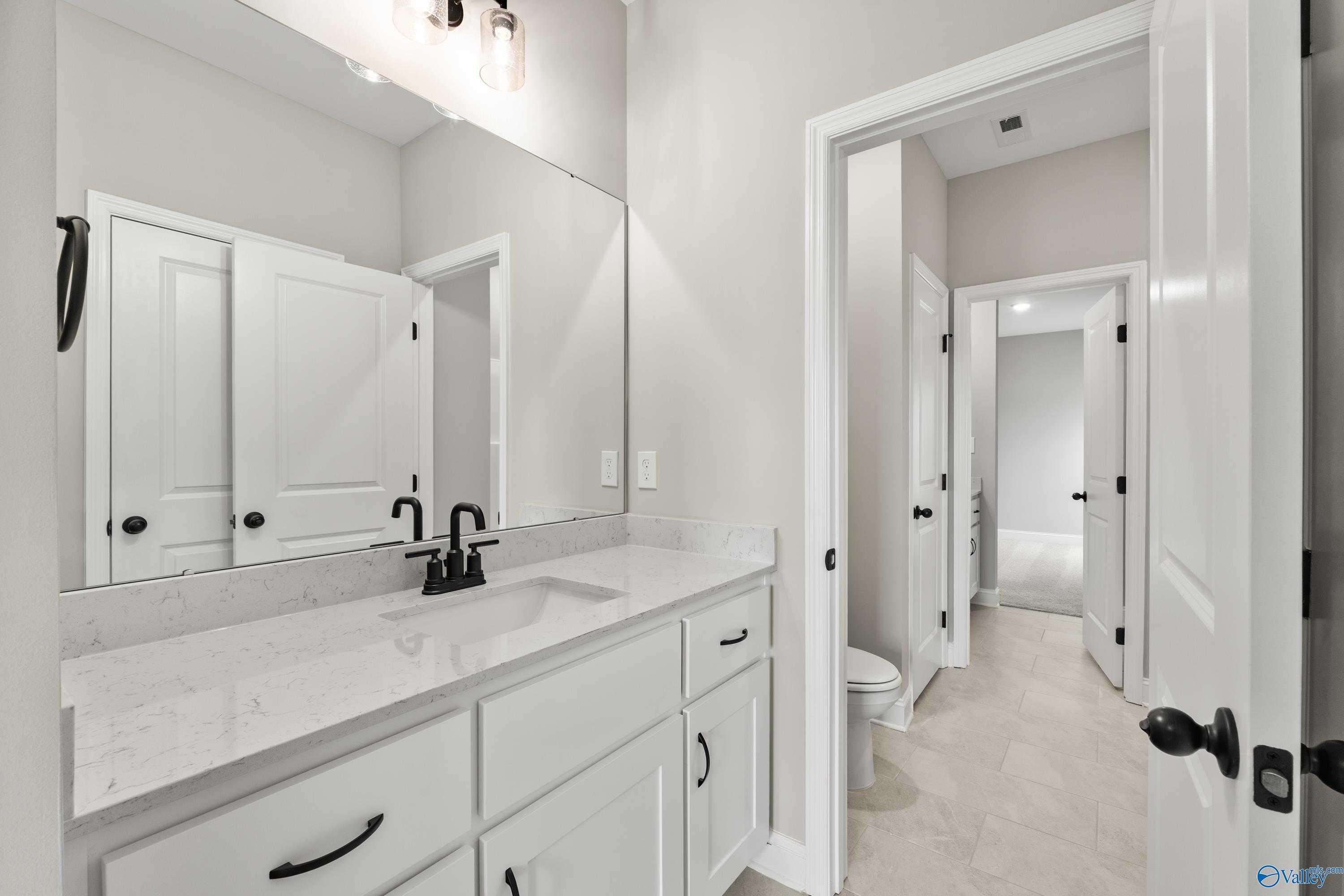 Modern bathroom with white shaker vanity, quartz countertop, black faucet, and adjacent bedroom in Davidson Homes The Finleigh, Toney, Alabama