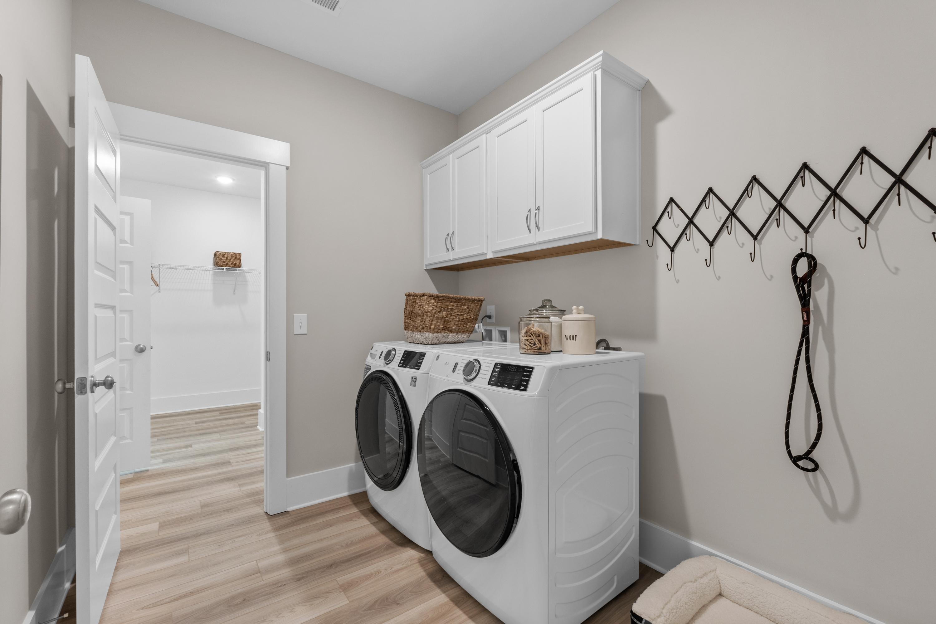 Modern laundry room at The Highlands in Arab, Alabama with white washer dryer, upper cabinets, wall hooks and luxury vinyl plank floors