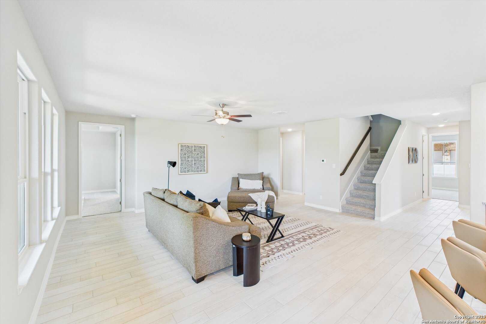 Spacious living room with beige sectional sofa, ceiling fan, staircase, and dining nook in The Jennings H 5-bedroom home, Ladera, San Antonio