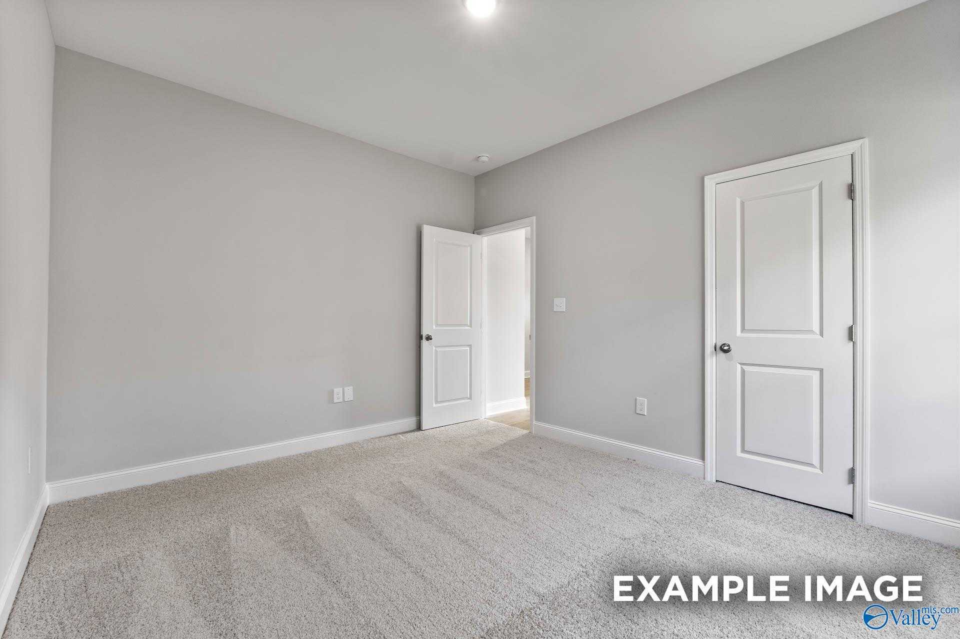 Spacious empty bedroom with light gray walls, white doors, and beige carpet in Davidson Homes The Daphne C, New Market, Alabama