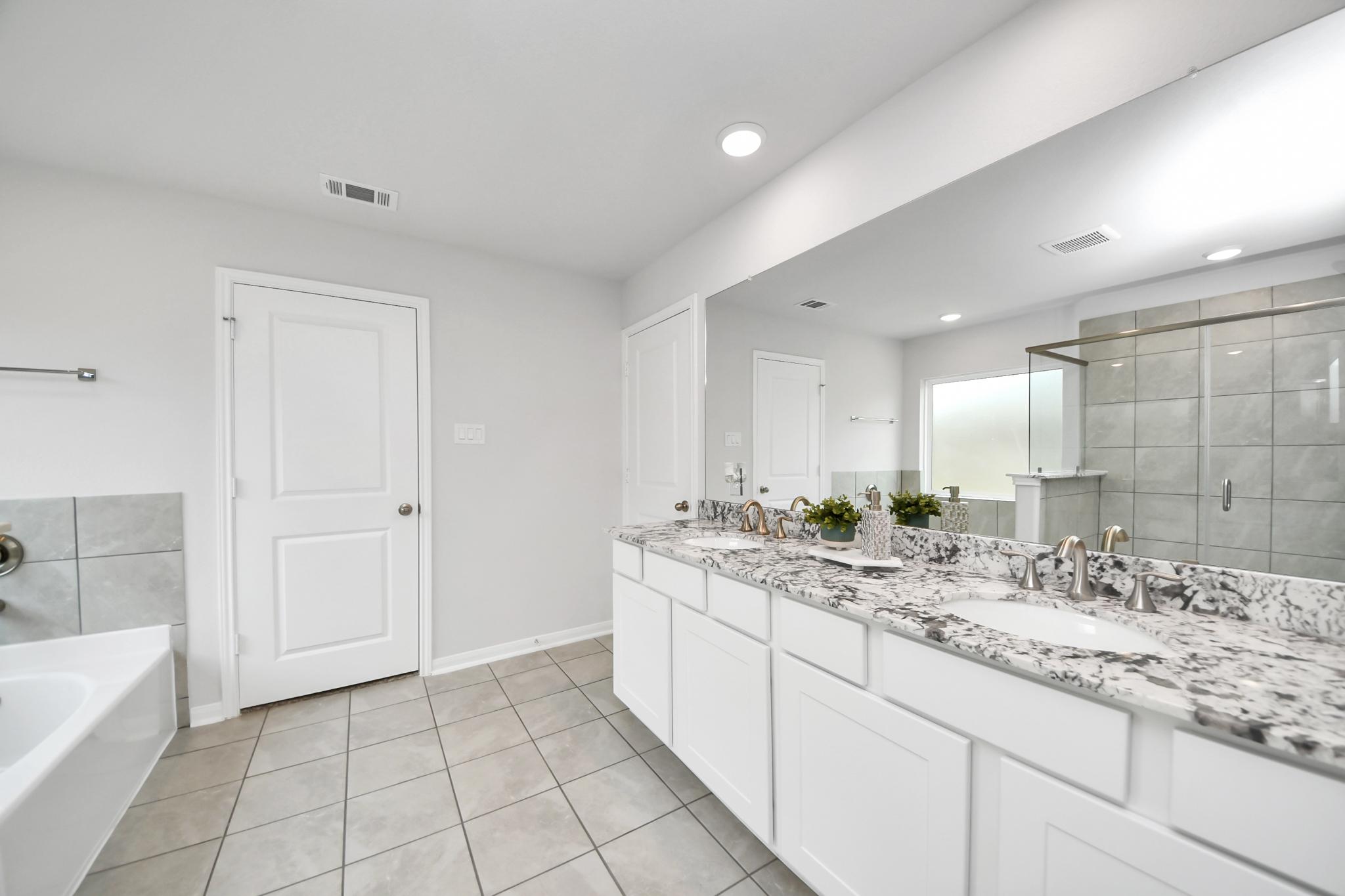 Primary bathroom with dual vanity, granite countertops, and tiled walk-in shower at Sunterra in Katy, TX by Davidson Homes.