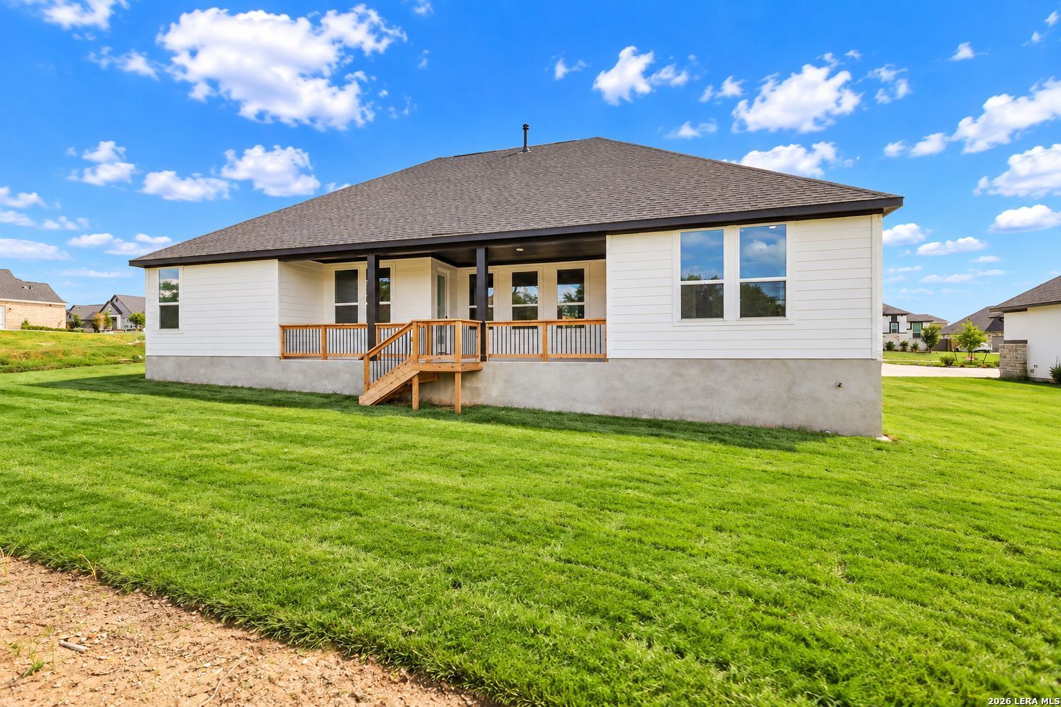 Rear exterior of white 1-story Davidson Homes Oxford F with covered porch and wooden deck in Potranco Oaks, Castroville, Texas