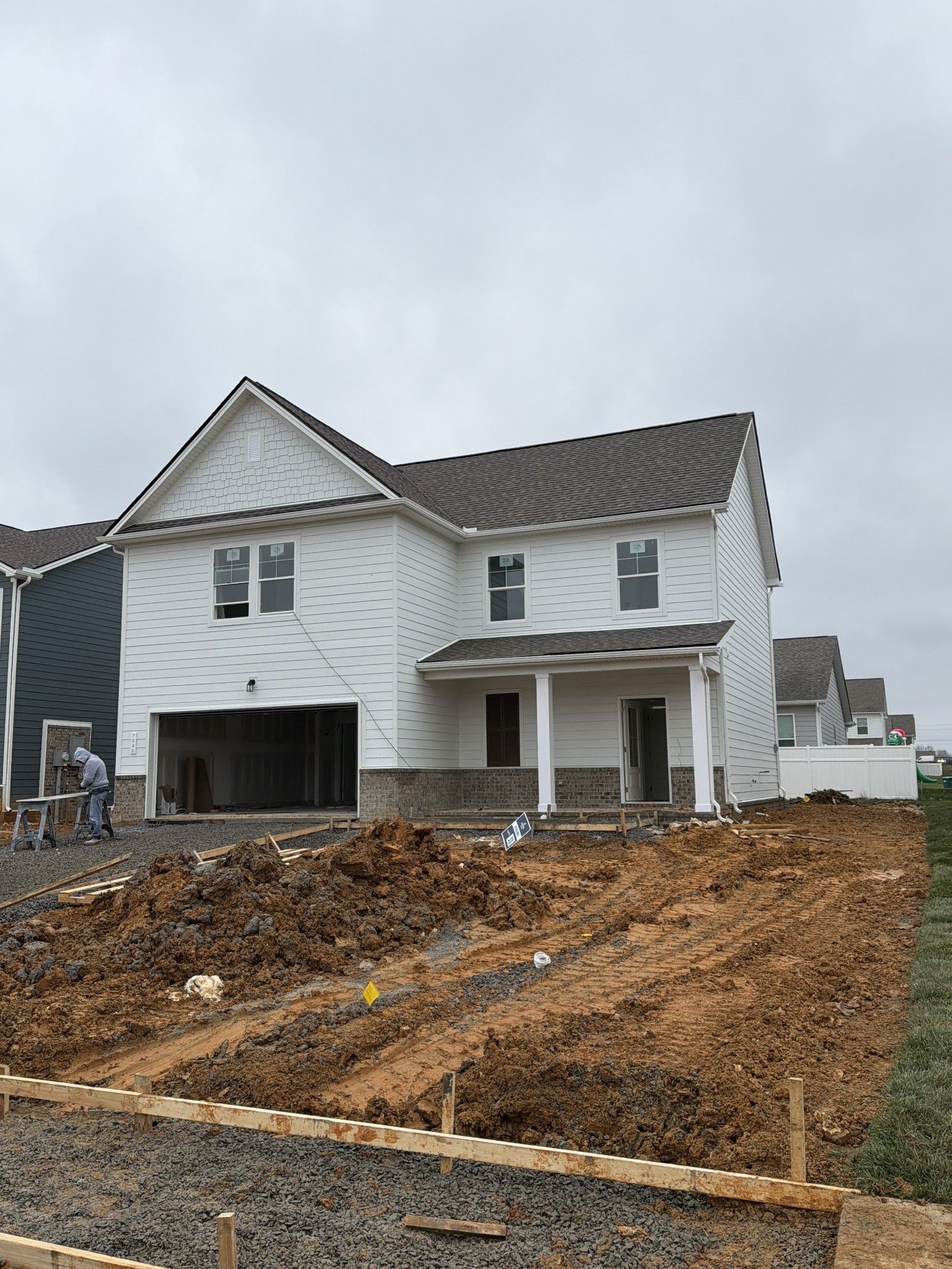 Two-story white home with dark shingle roof, open 2-car garage, front porch, and yard construction in Sage Farms, White House, TN