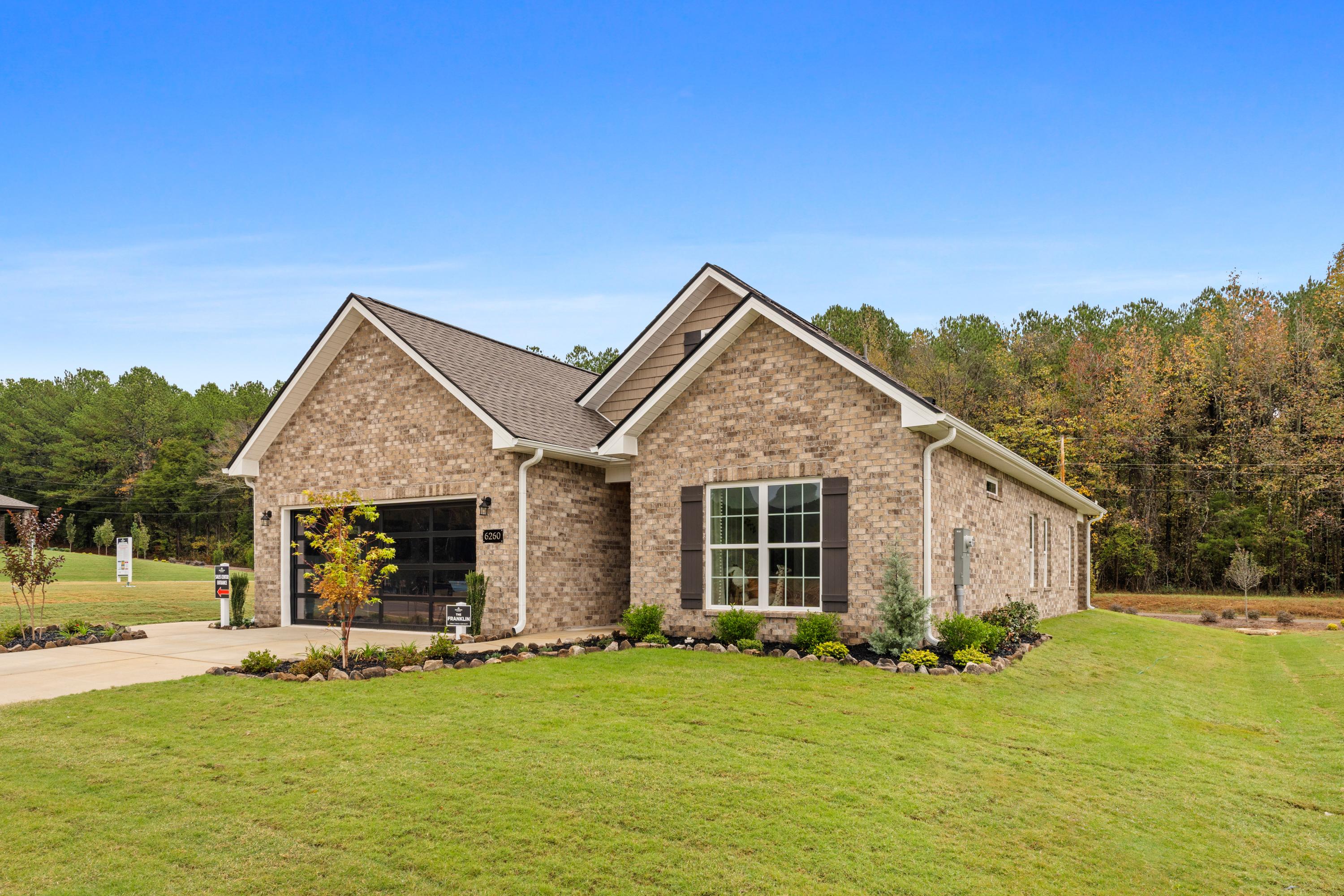 Brick ranch home exterior at Spragins Cove in Huntsville AL with attached garage, large windows, and lush green landscaping