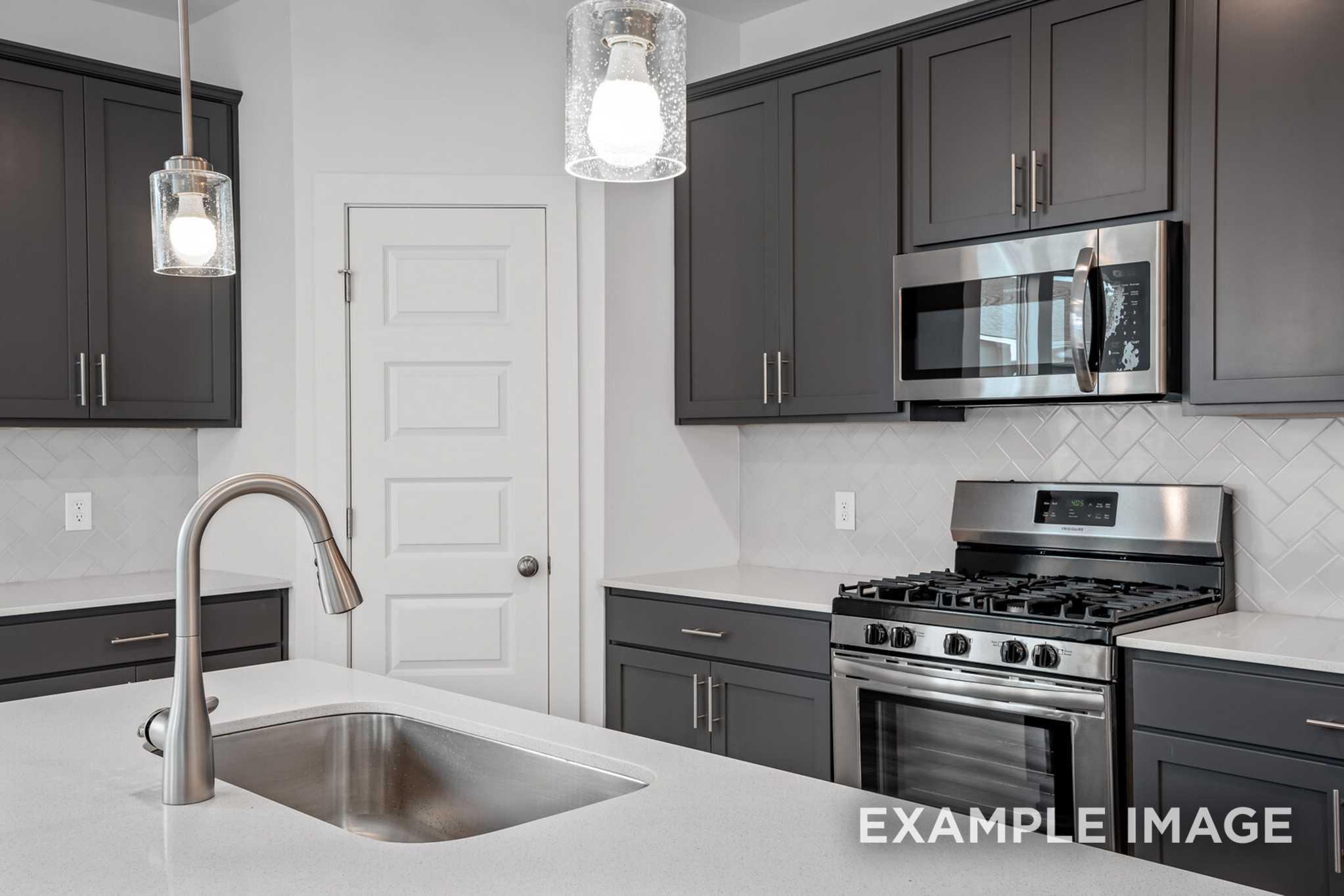Modern kitchen in The Murray B featuring dark cabinets, stainless steel appliances, subway tile backsplash