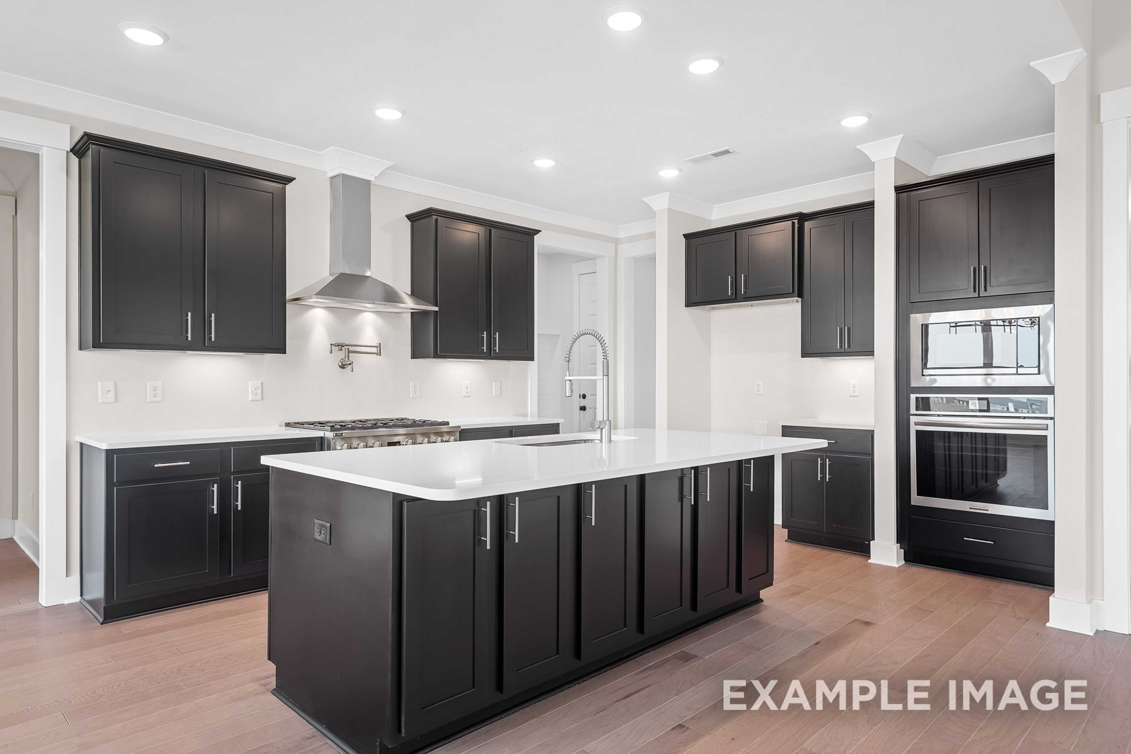 Spacious modern kitchen in The Hawkins with dark shaker cabinets, quartz island, gas range, double ovens, and hardwood floors