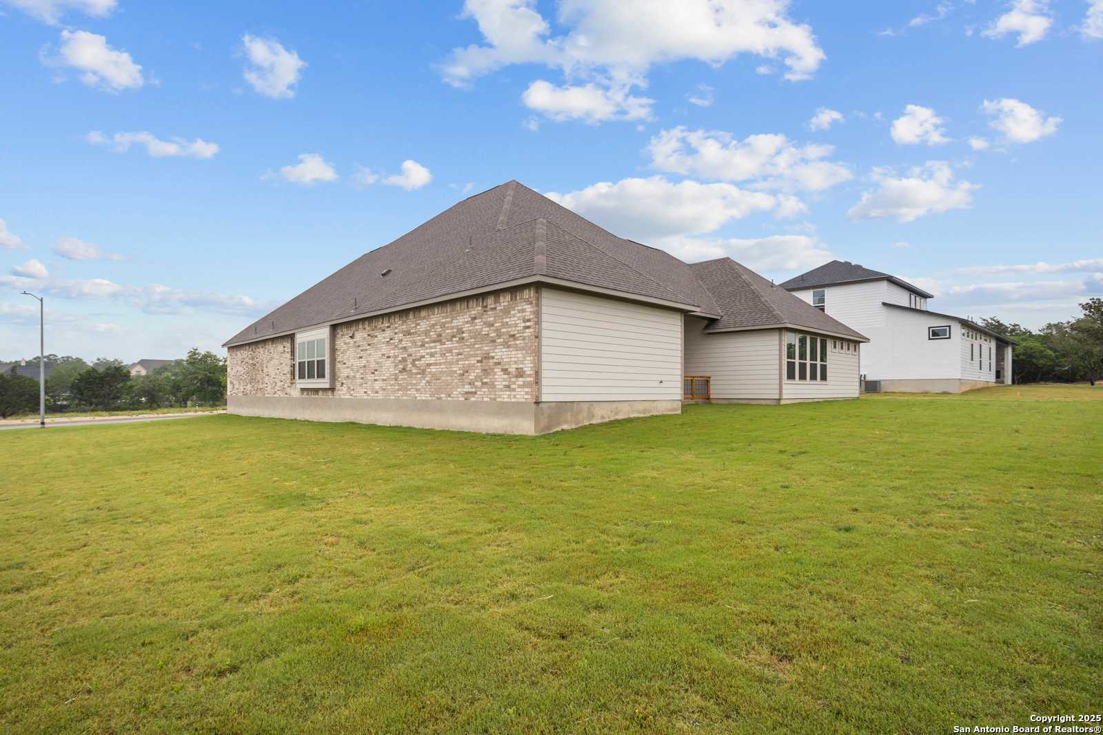 Modern single-story home exterior with stone accents, white siding, and lush green lawn in Potranco Oaks, Castroville, Texas