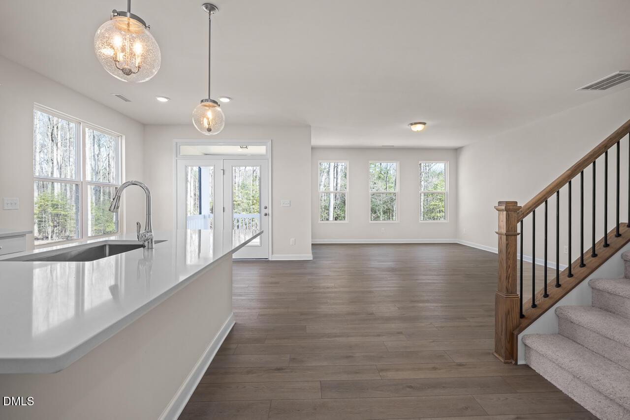 Open-concept kitchen with quartz island, stainless sink, and pendant lights flowing to living area and staircase in The Ash B home, Lillington, NC