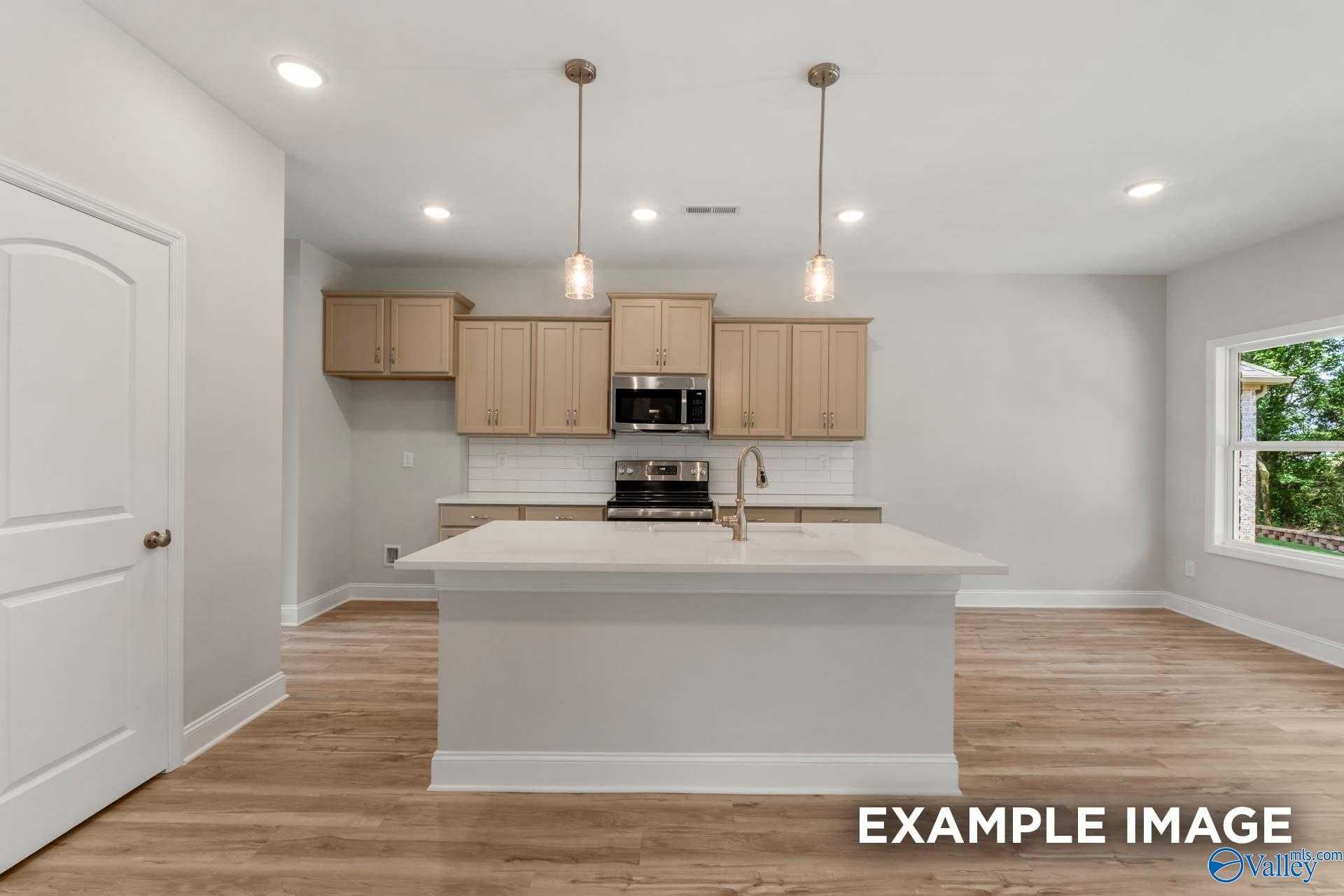 Modern kitchen featuring white island, stainless appliances, subway tile backsplash, and hardwood floors in The Shelby C, Meridianville
