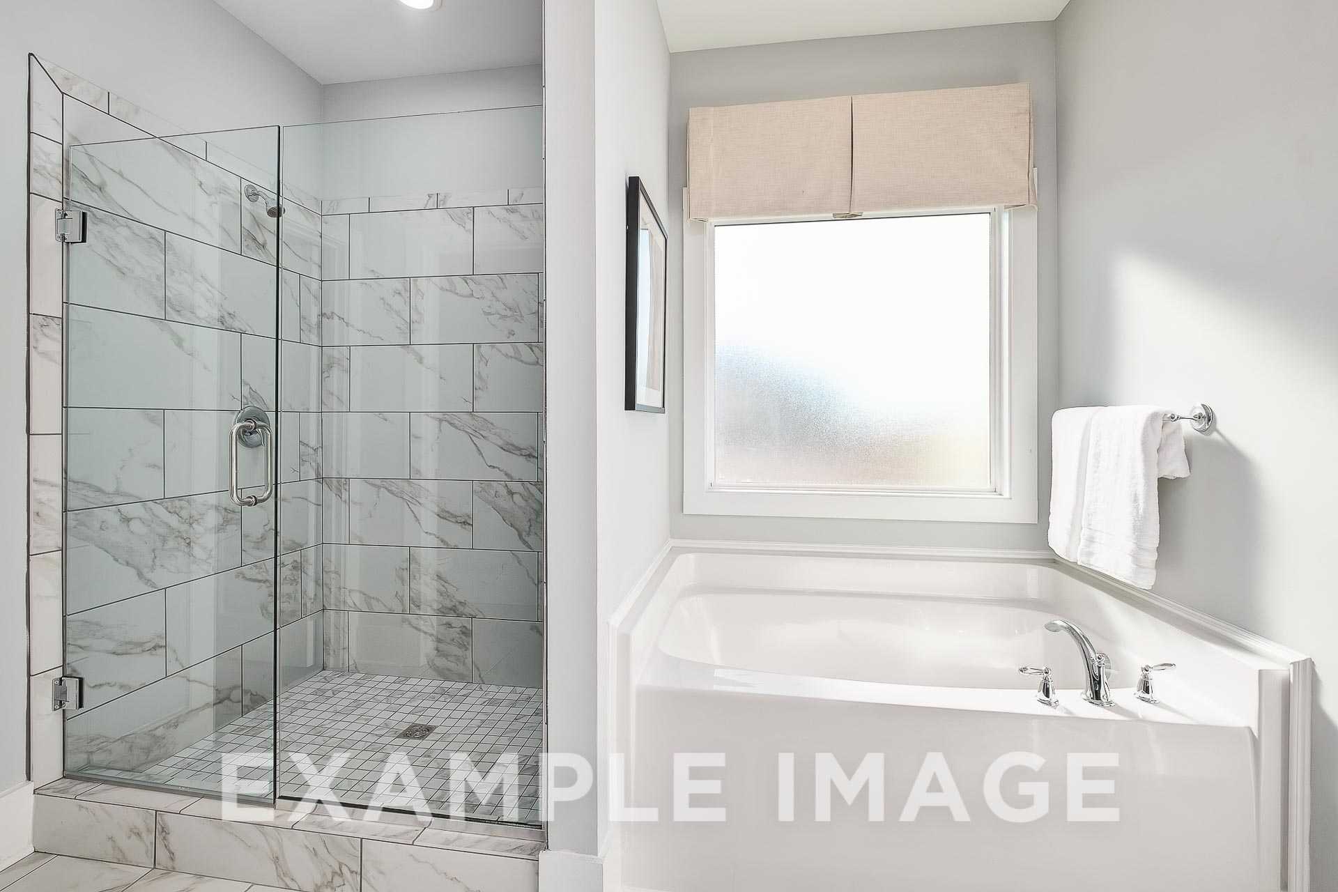 Spacious master bathroom in The Everett B with frameless glass shower, subway tile surround, deep soaking tub, and frosted window