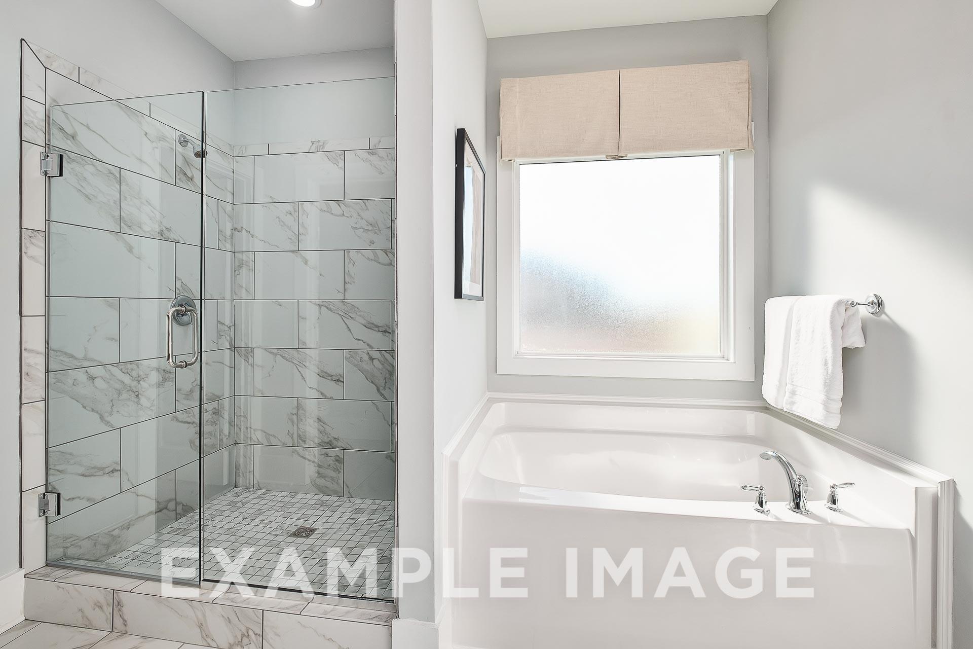 Spacious master bathroom in The Everett B with frameless glass shower, subway tile surround, deep soaking tub, and frosted window