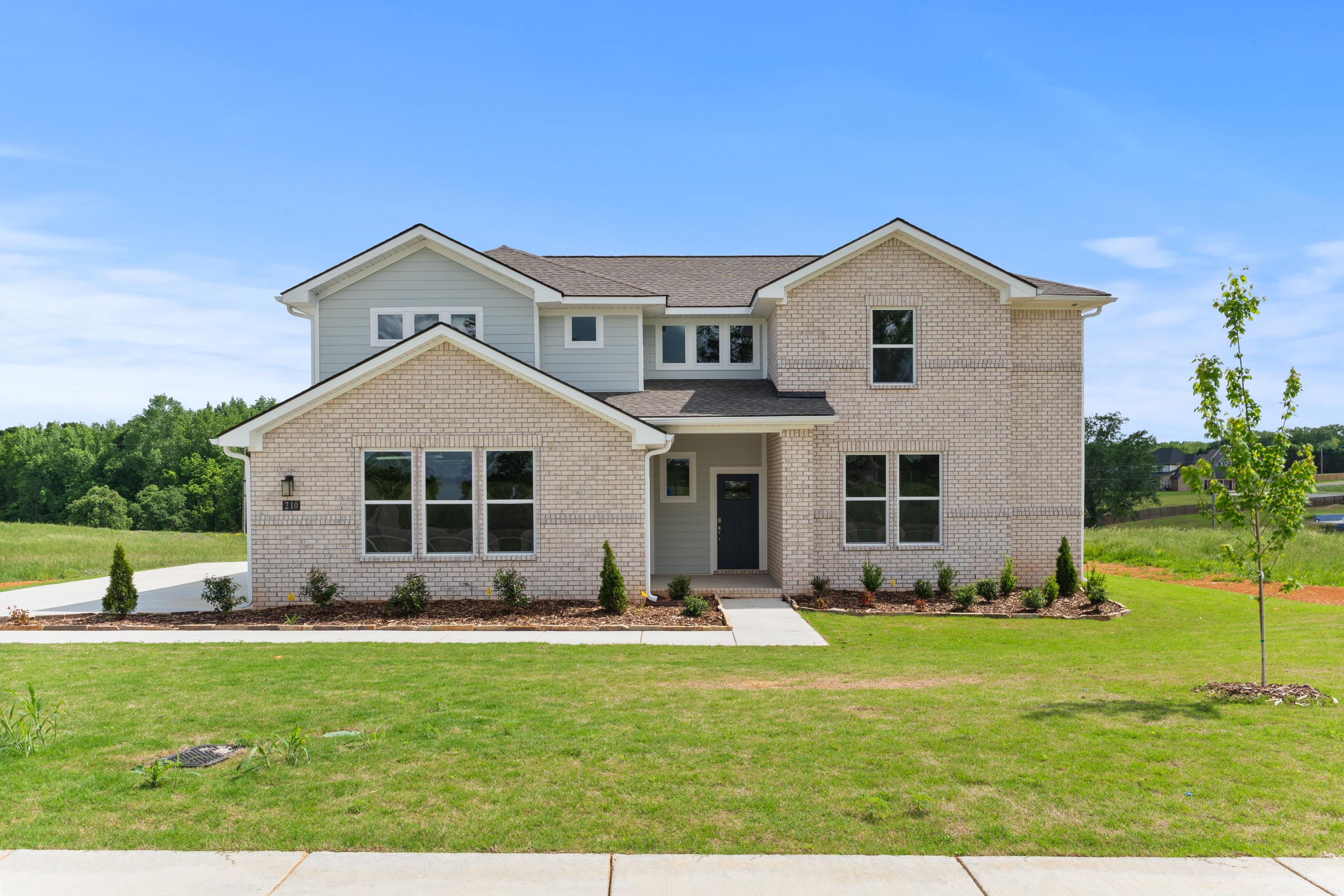 Modern brick ranch-style elevation of The Haven E home featuring large windows, covered porch, and lush green lawn in Owens Cross Roads