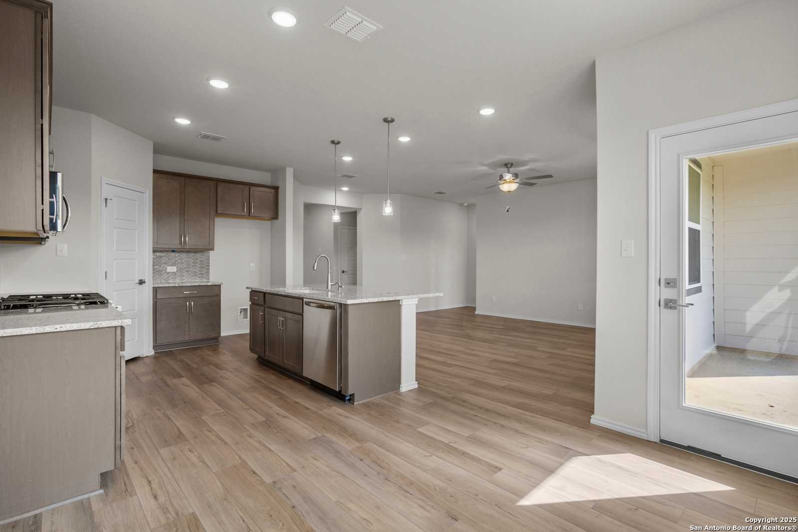 Open-concept kitchen with taupe cabinets, large center island, stainless dishwasher, and wood flooring in Davidson Homes The Asheville J, San Antonio