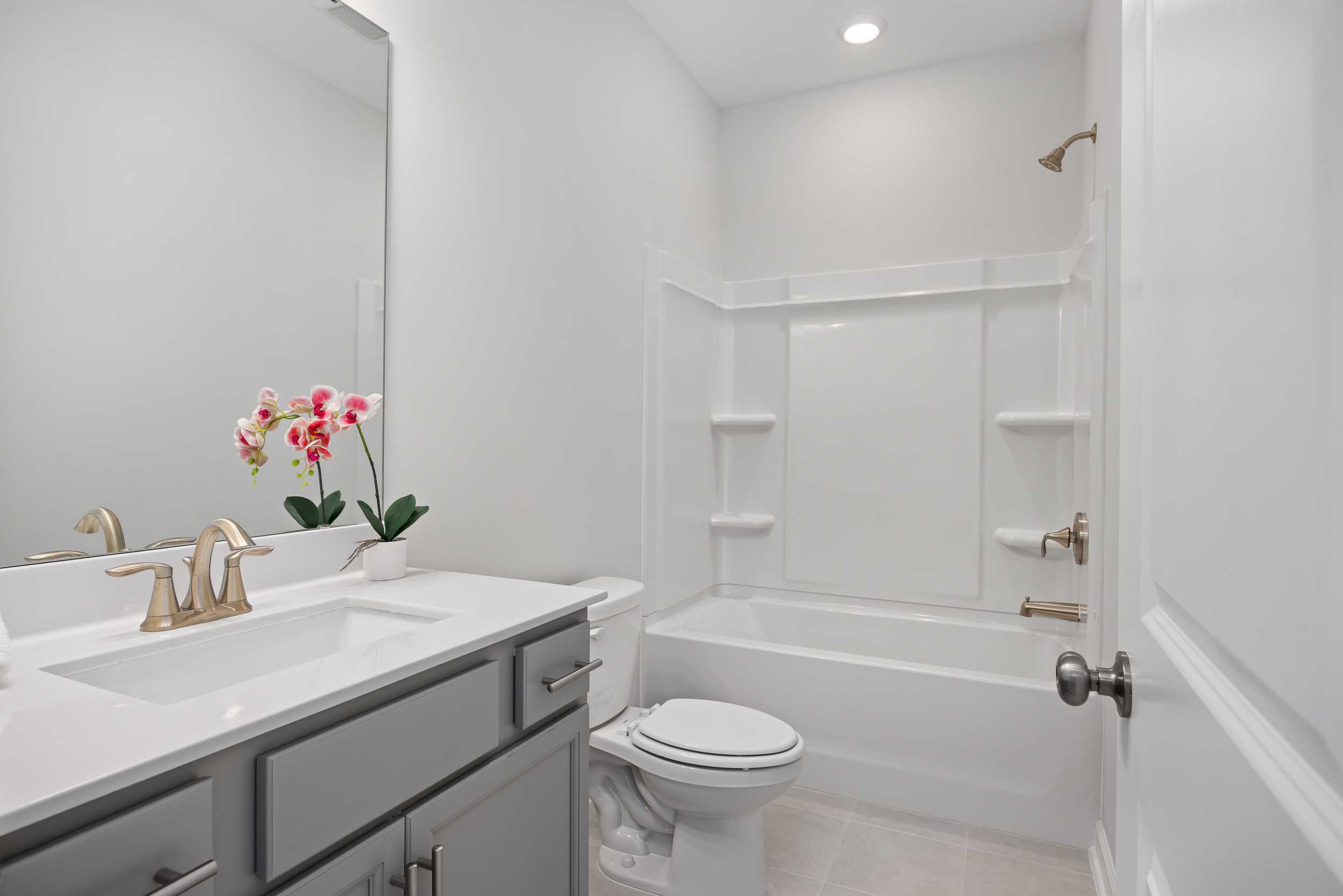 Spacious bathroom in The Daphne C home design featuring white tub, dual sink vanity, gray cabinets, and pink orchids