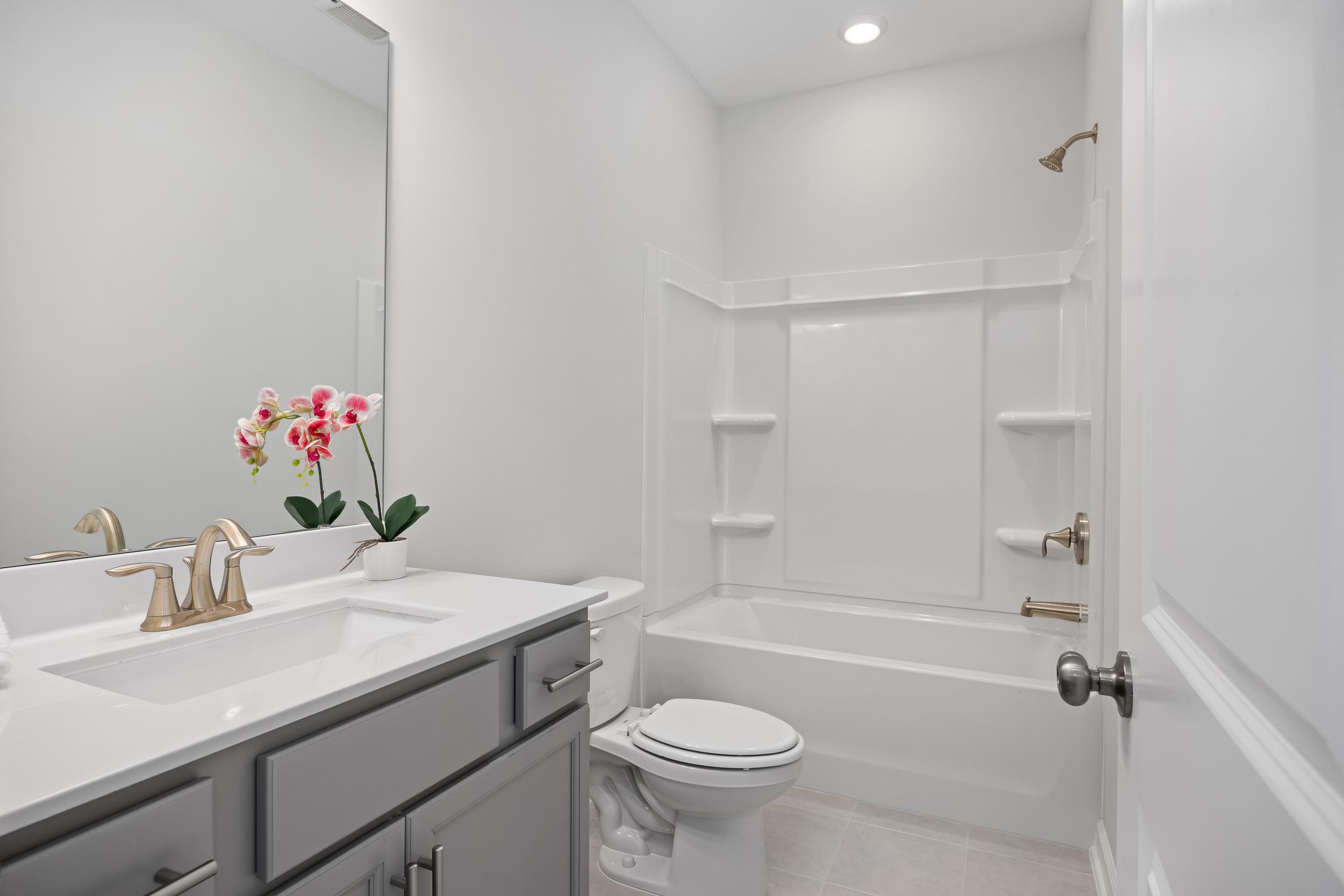 Modern secondary bathroom in The Daphne D featuring white tub-shower combo, double sink vanity, and pink orchids