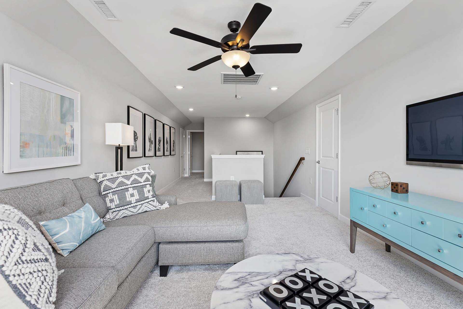 Cozy loft bonus room at Bentwinds in Fuquay-Varina NC with gray L-shaped sofa, ceiling fan, wall TV and modern decor