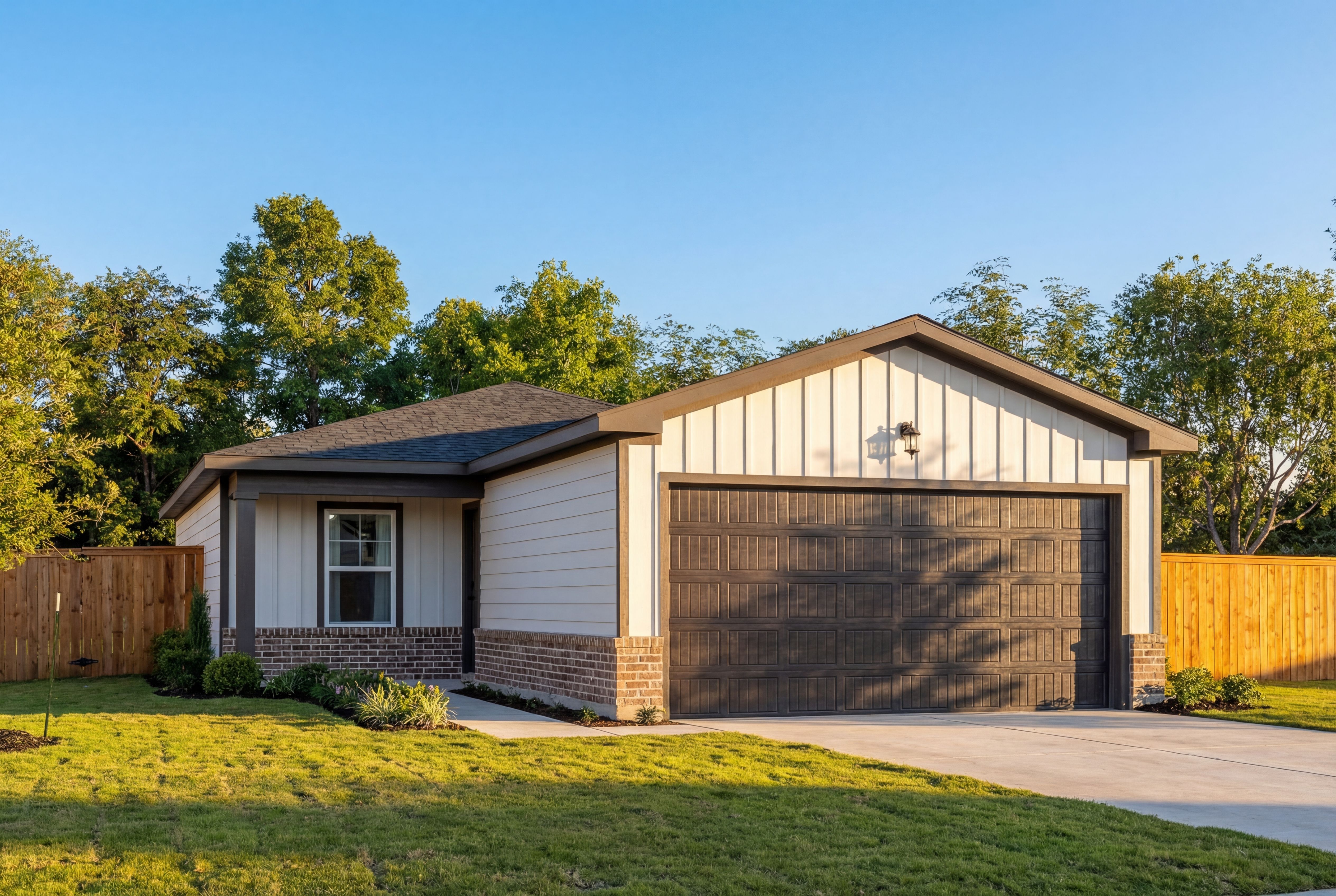 Modern single-story elevation of The Comal B with white siding, brick accents, dark 2-car garage, and landscaped yard in San Antonio