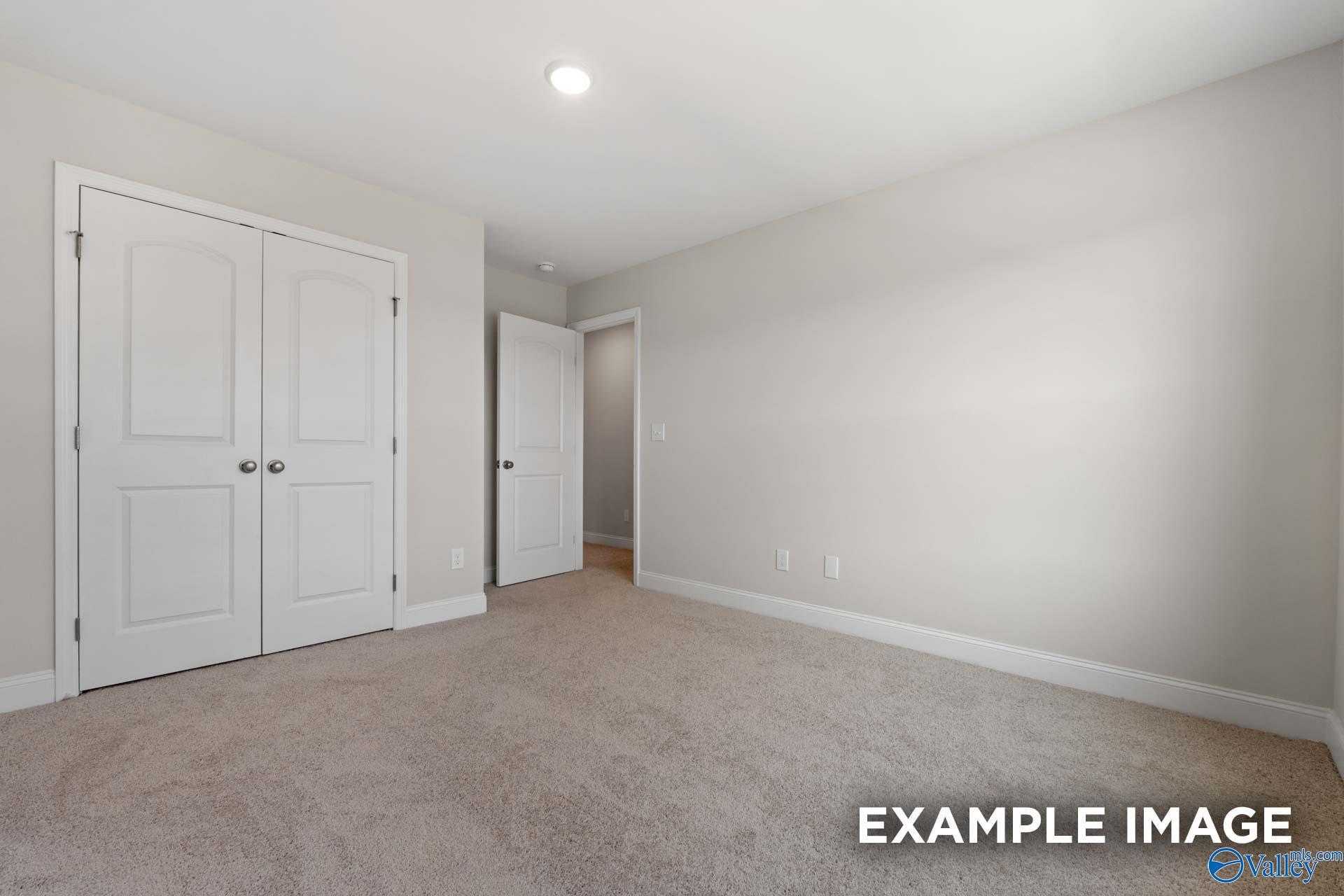 Empty bedroom with beige carpet, double white closet doors, and light gray walls in Davidson Homes Madison A, Toney, Alabama