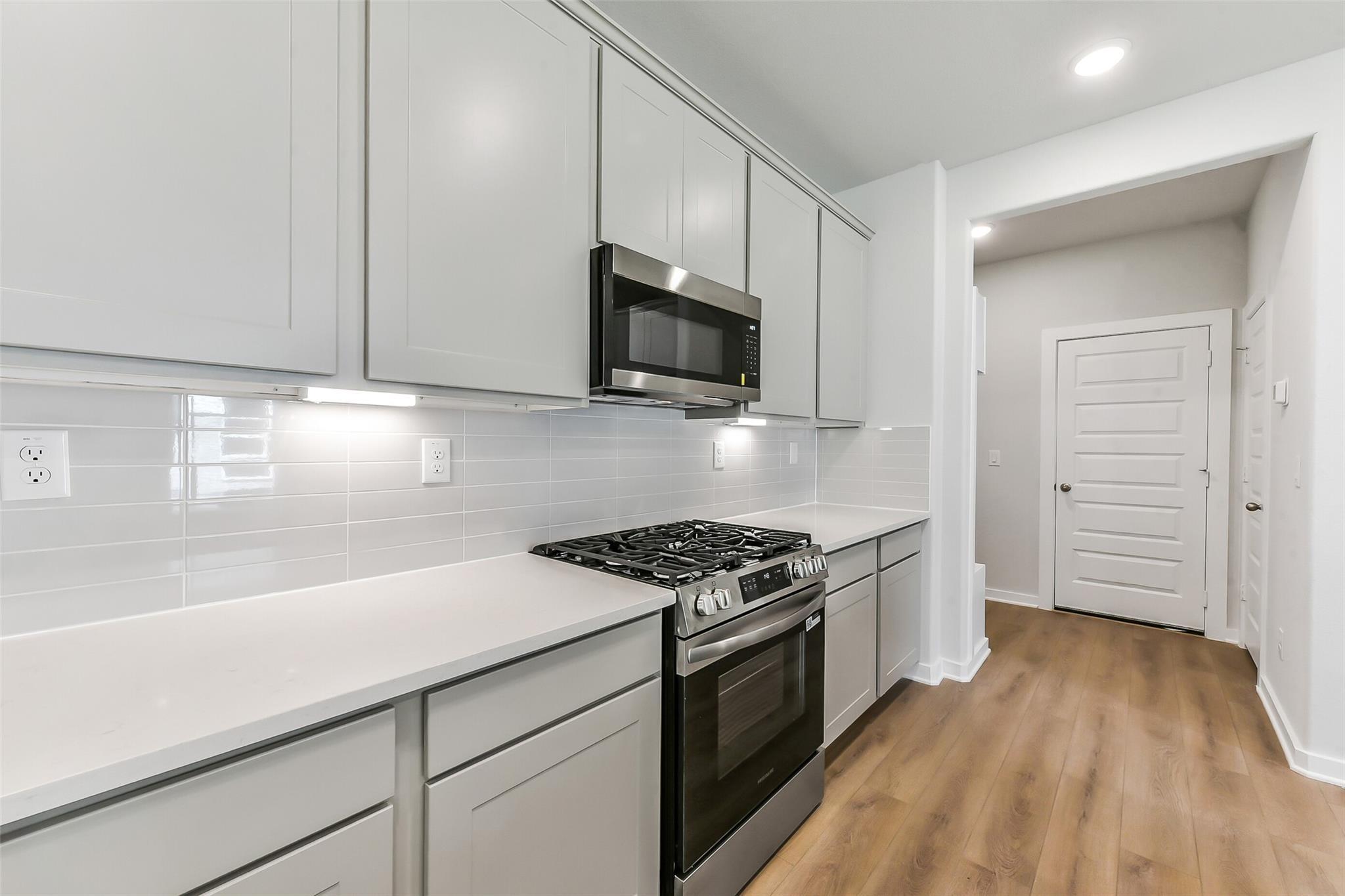 Modern kitchen featuring white shaker cabinets, stainless steel gas range, and subway tile backsplash in Davidson Homes The Brazos E, Magnolia, Texas