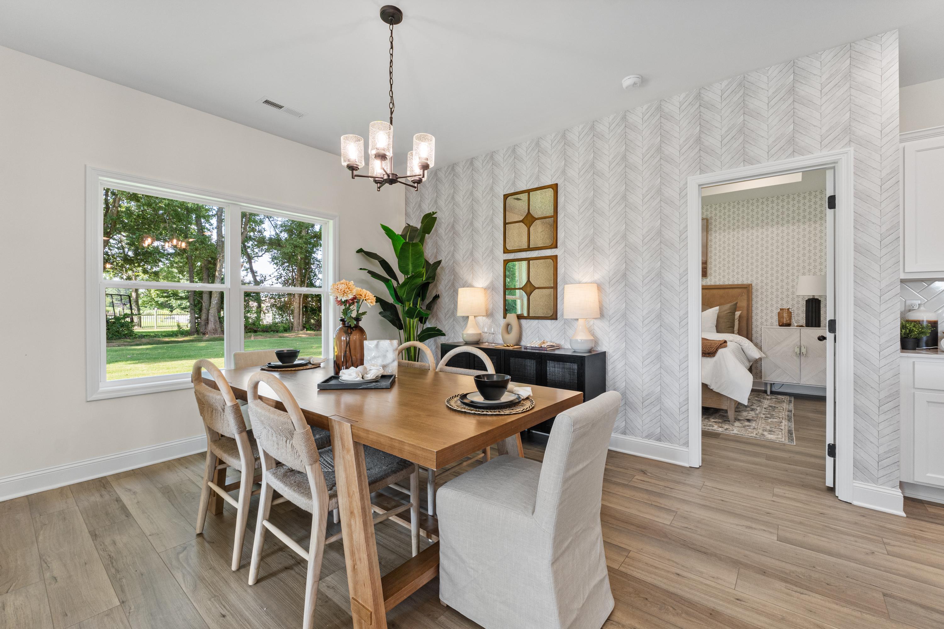 Elegant dining room at Lynn Meadows in Meridianville AL with wooden table, chandelier, potted plants, and large window views