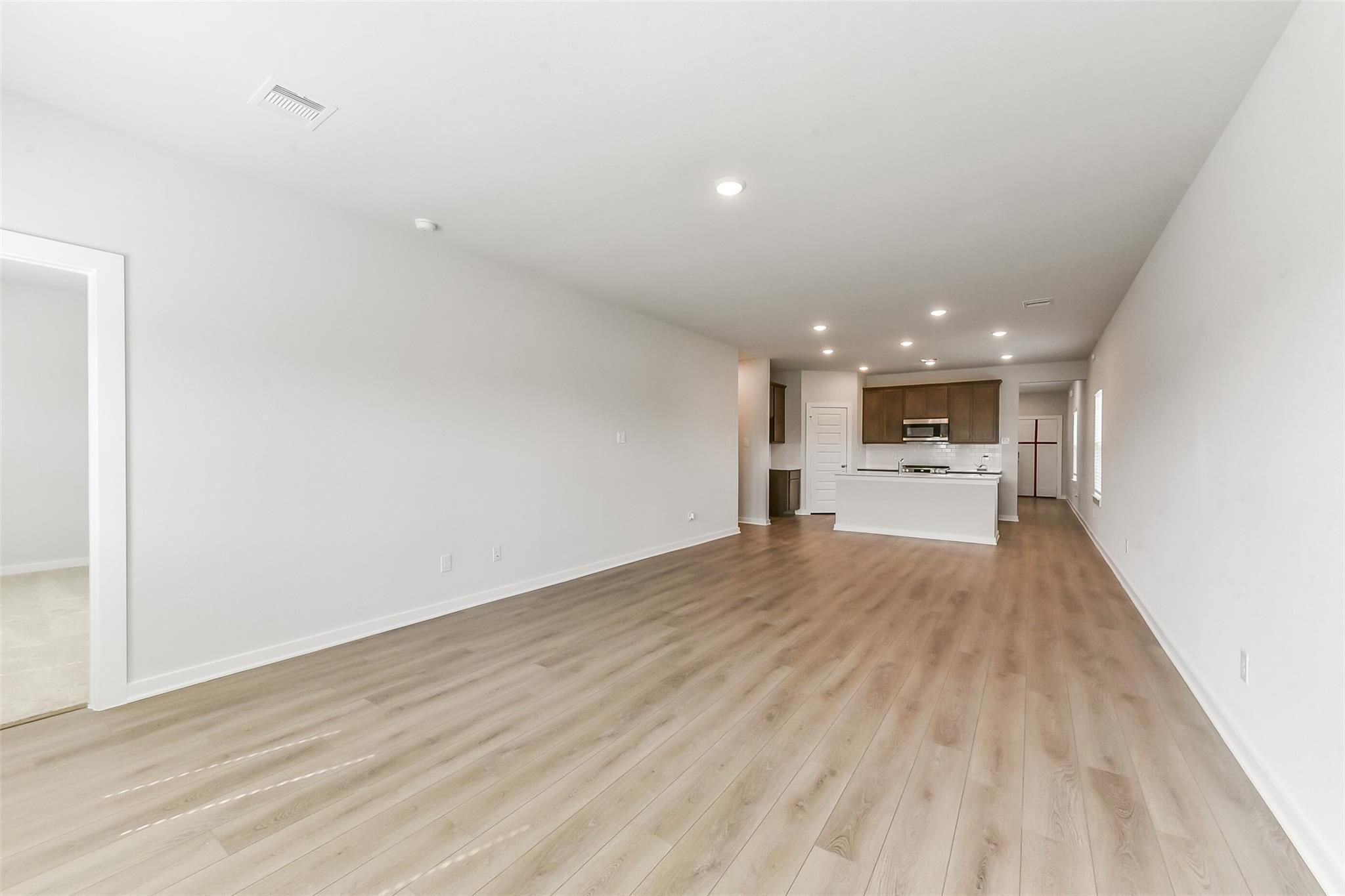 Open-concept living and kitchen area with light oak floors, white cabinet island, and recessed lights in Sabine F home, Dayton, Texas