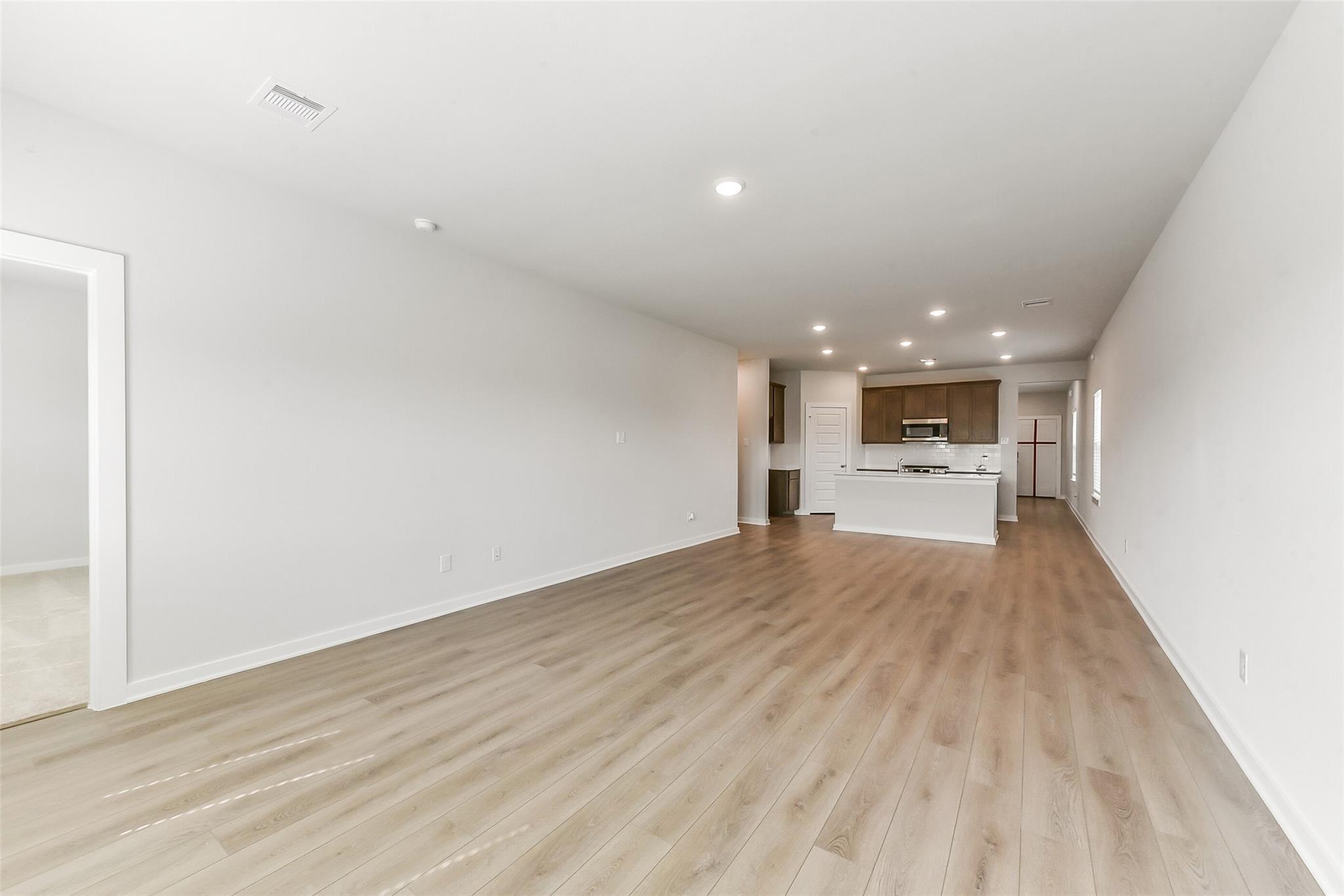 Open-concept living and kitchen area with light oak floors, white cabinet island, and recessed lights in Sabine F home, Dayton, Texas