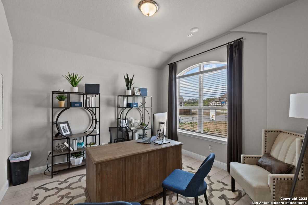Stylish home office with wooden desk, blue chair, bookshelves, plants, and arched window in Davidson Homes The Garner B, Ladera, San Antonio