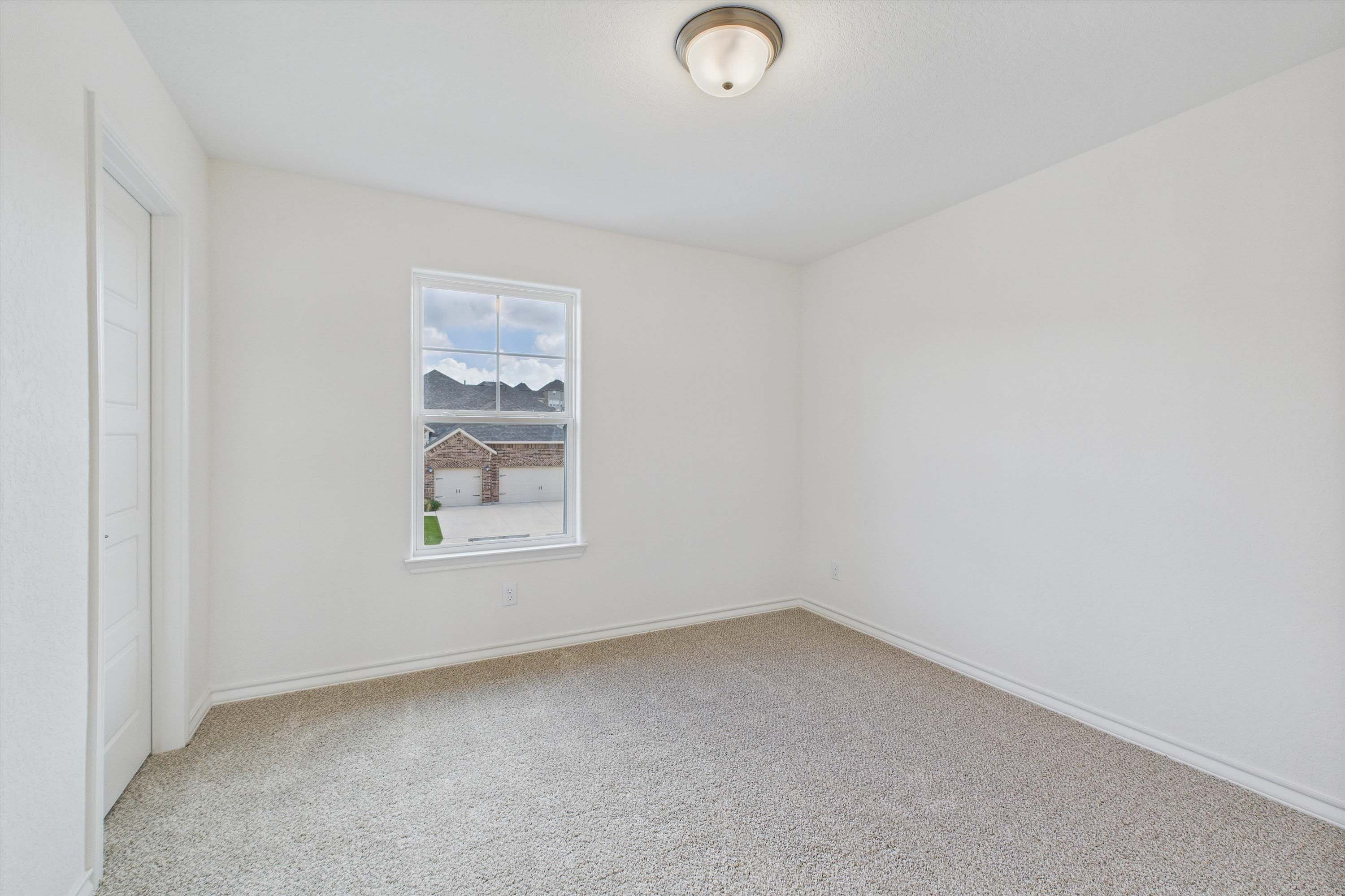 Spacious bedroom with neutral carpet in The Danbury home design by Davidson Homes, featuring bright walls and window view.