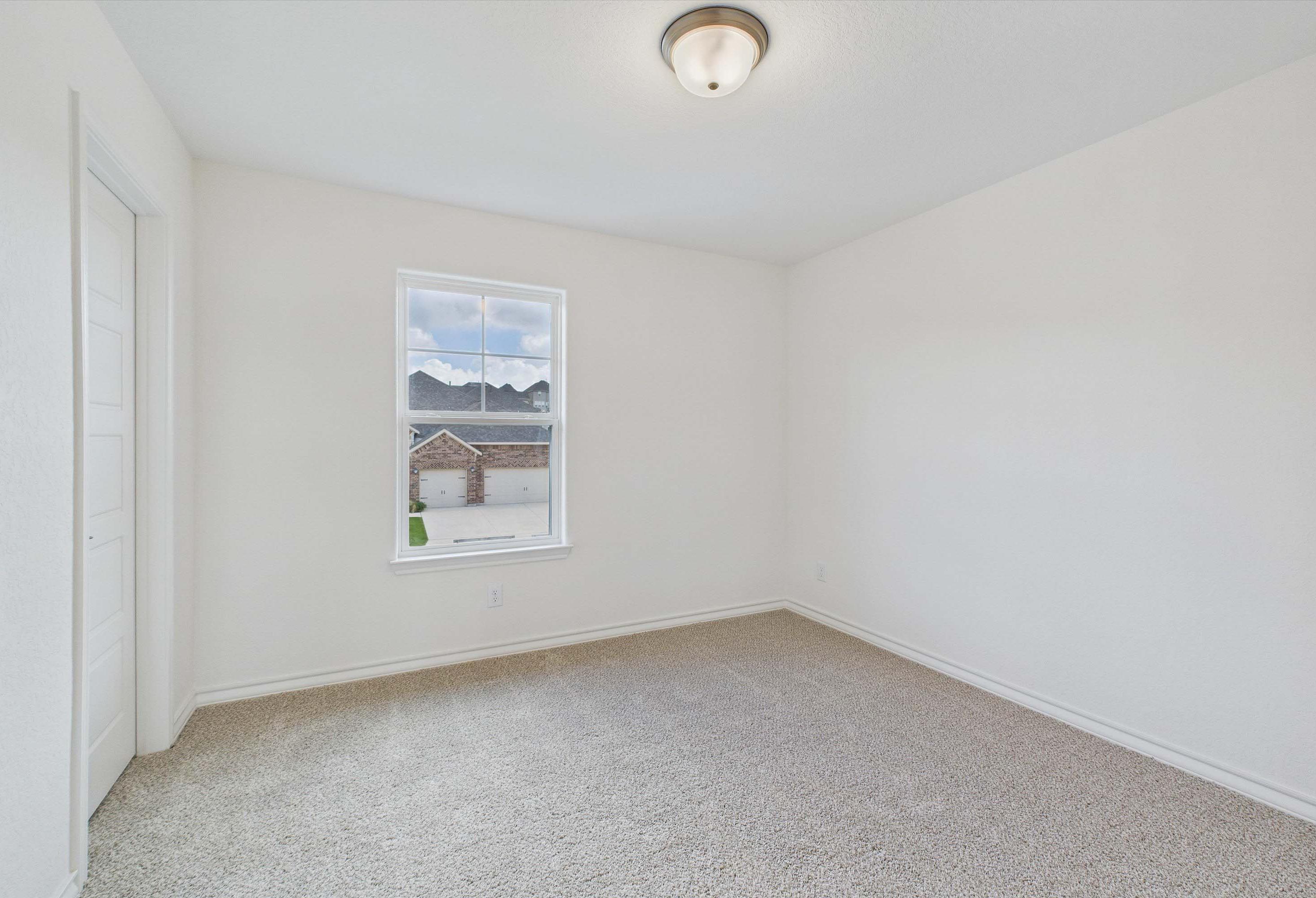 Spacious bedroom with neutral carpet in The Danbury home design by Davidson Homes, featuring bright walls and window view.