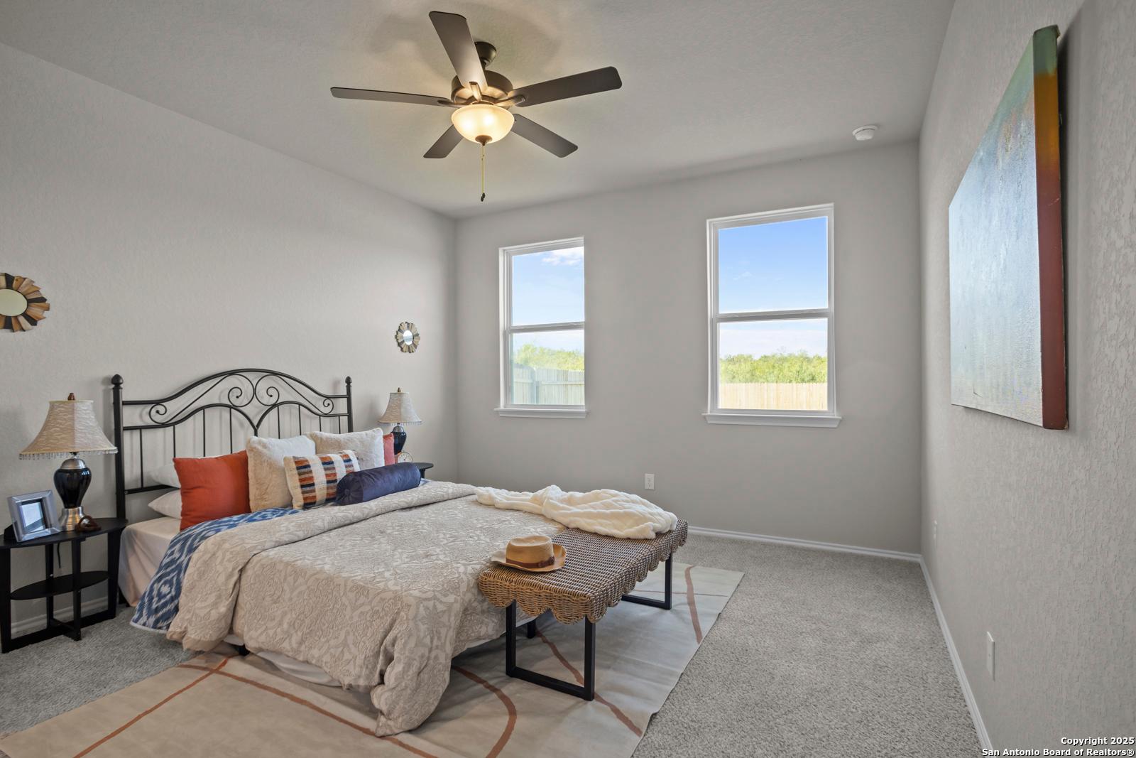 Cozy bedroom with iron bed, ceiling fan, large windows, and abstract wall art in Davidson Homes The Asheville H, Converse, Texas