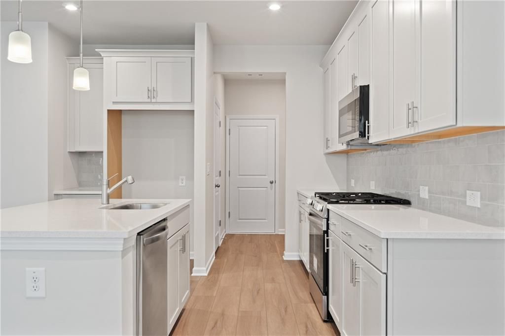 Modern white kitchen with large island, stainless steel appliances, subway tile backsplash in Davidson Homes The Marion B, Kennesaw, GA