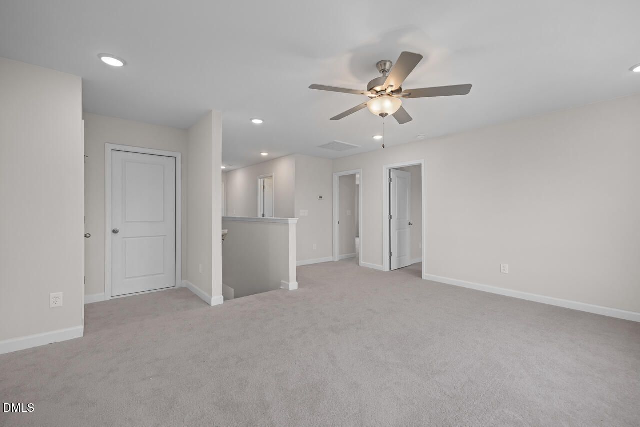 Spacious upstairs hallway with beige carpet, white doors, ceiling fan, and railing in 4-bedroom The Cypress D II home, Angier NC