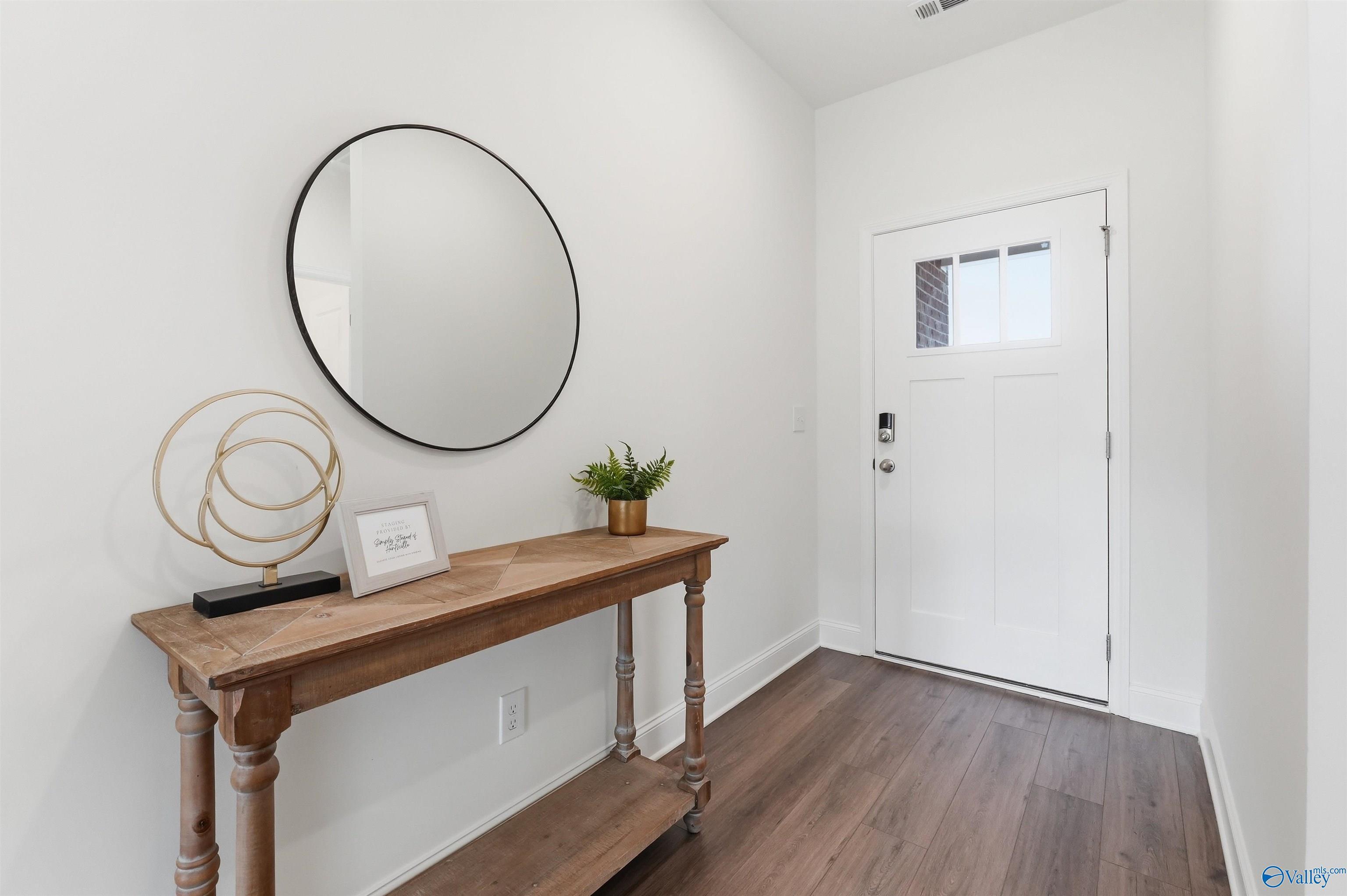 Modern entryway with rustic wood console table, round mirror, and white door in The Franklin C home at Lynn Meadows.