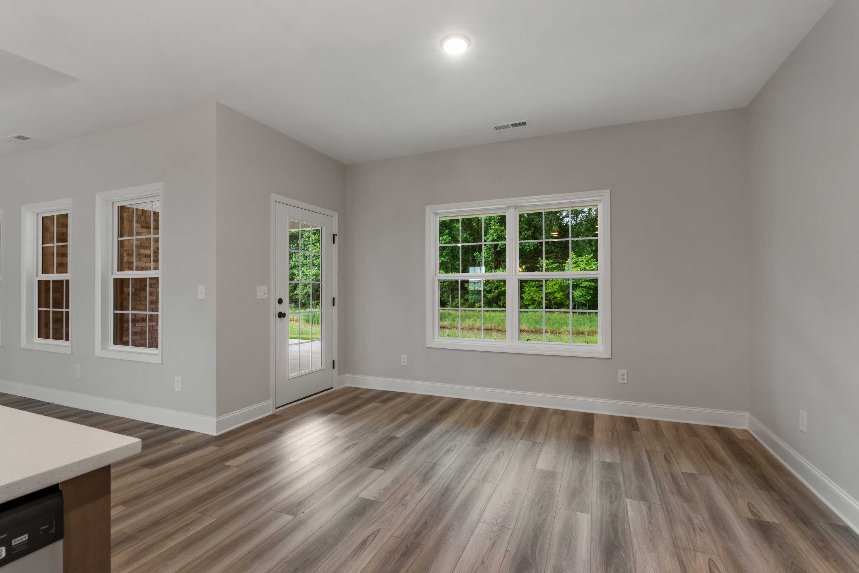 Bright living room in The Oxford home design featuring gray walls, large windows with greenery view, French door, and hardwood floors