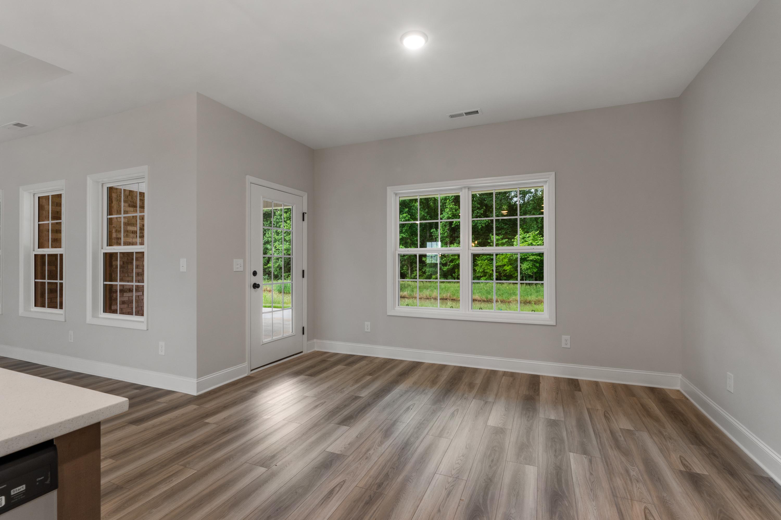 Bright living room in The Oxford home design featuring gray walls, large windows with greenery view, French door, and hardwood floors
