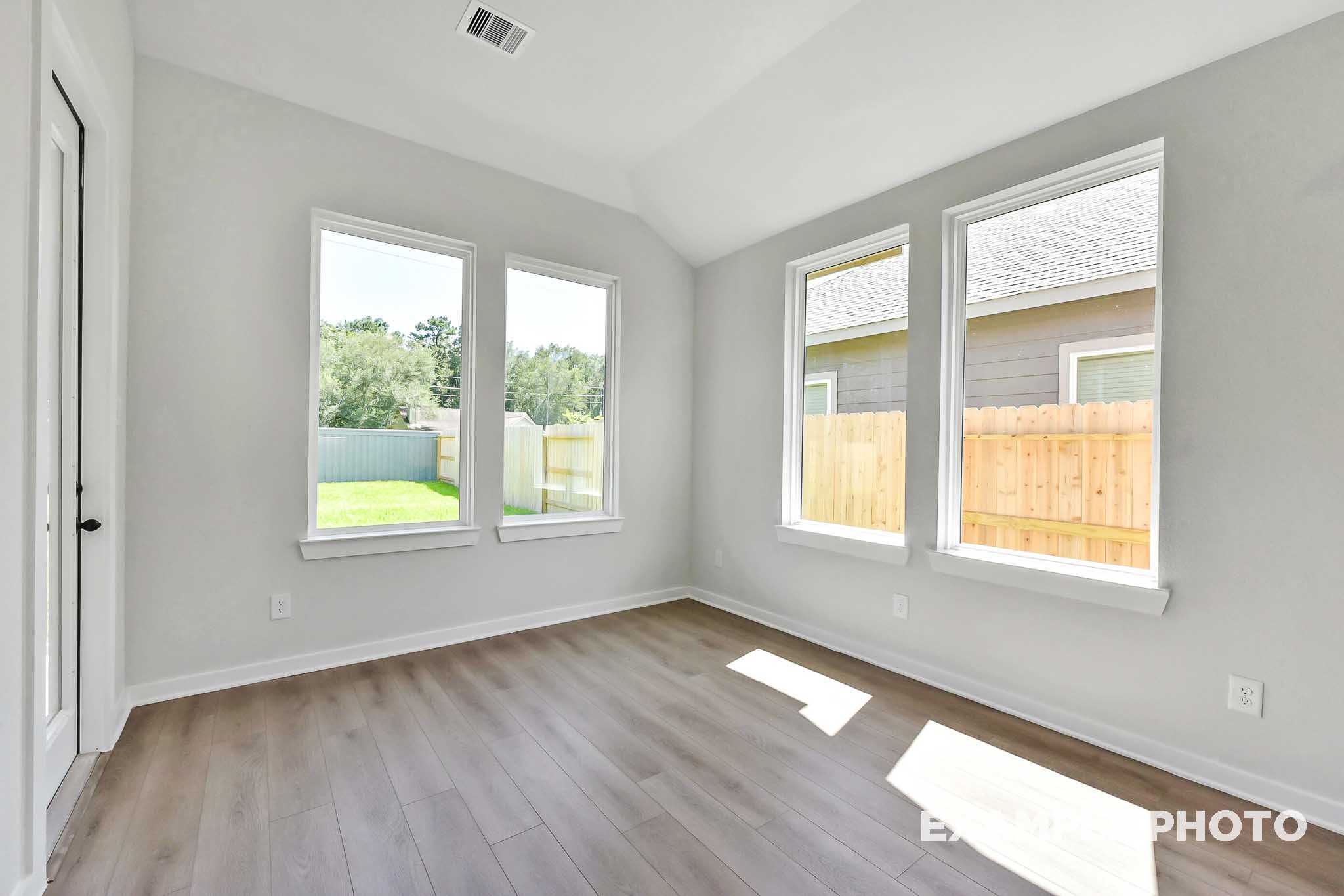 Bright master bedroom in The Sequoia home with vaulted ceiling, large windows, hardwood floors, and backyard view