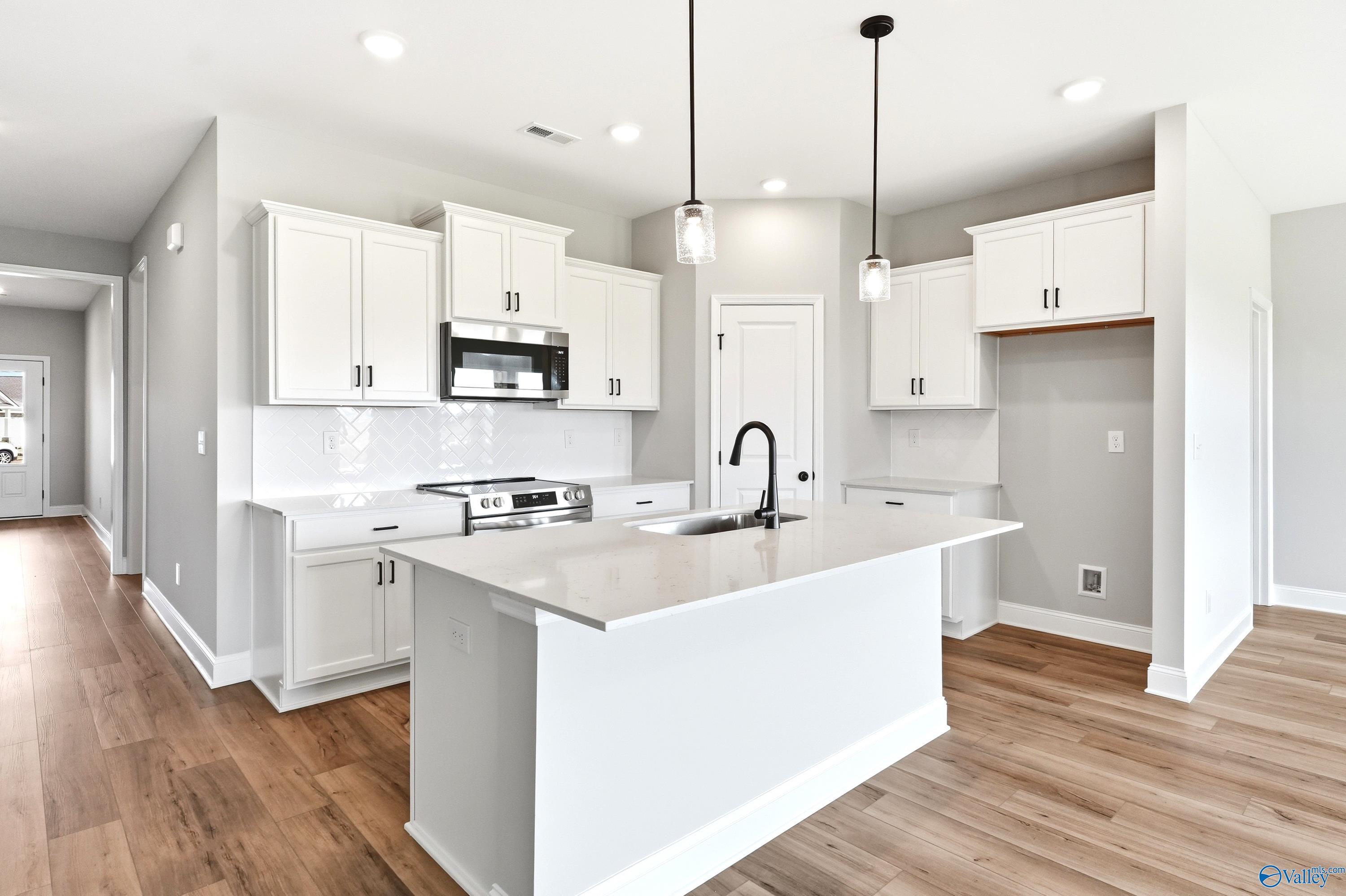 Modern kitchen with white cabinets, quartz island, and stainless appliances in The Daphne D floor plan, Creekside, Harvest.