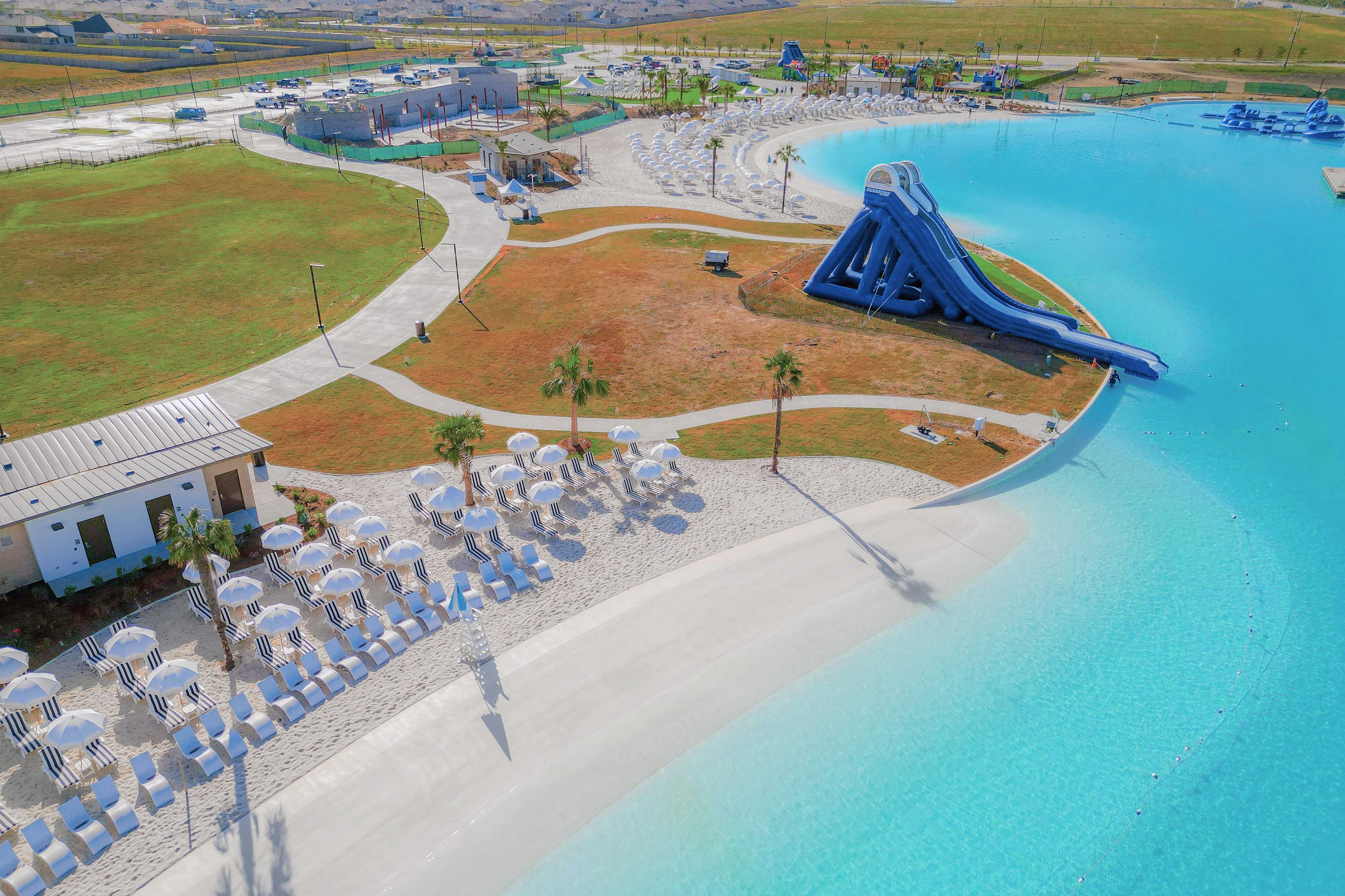 Resort-style lagoon pool at River Ranch Meadows in Dayton Texas with blue water slide, sandy beach, and umbrella loungers