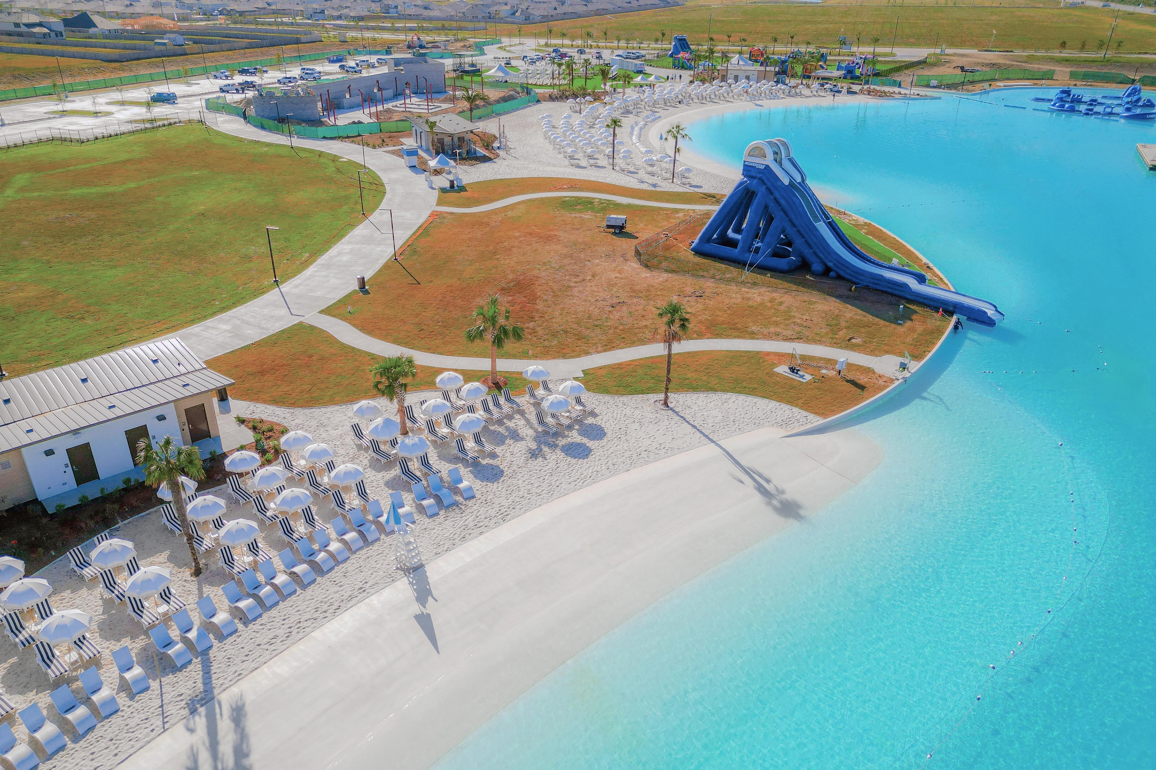 Resort-style lagoon pool at River Ranch Meadows in Dayton Texas with blue water slide, sandy beach, and umbrella loungers