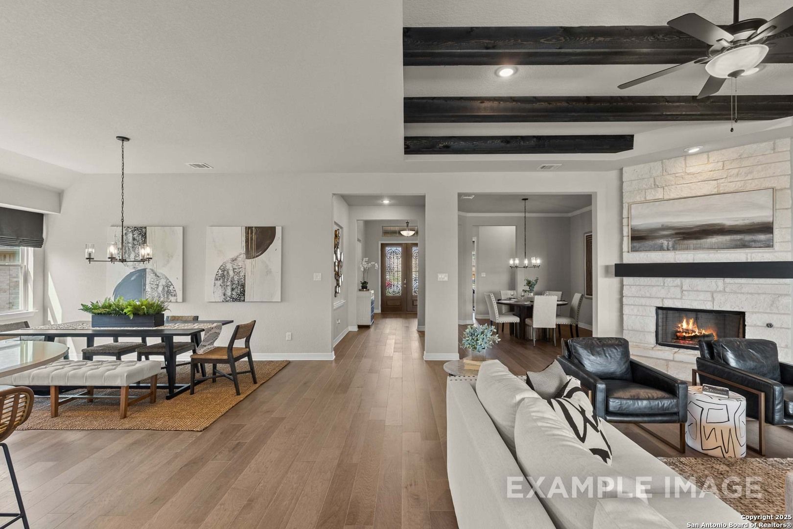 Spacious open great room with beamed ceiling, stone fireplace, dining table, and leather seating in Davidson Homes Summerlin B, Castroville