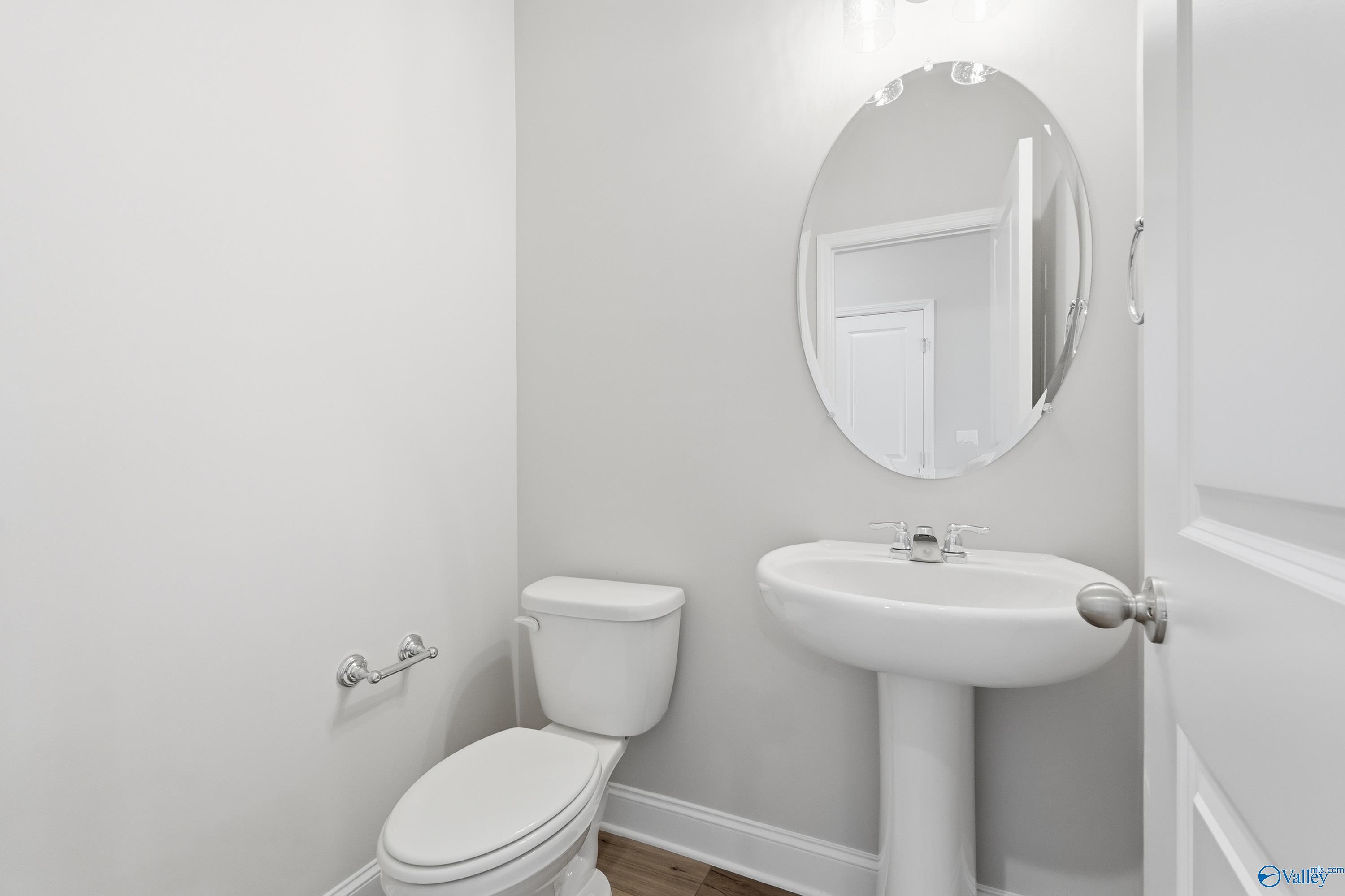 Elegant powder room with pedestal sink, round mirror, and white toilet in Davidson Homes The Rockford, Creekside, Harvest, Alabama