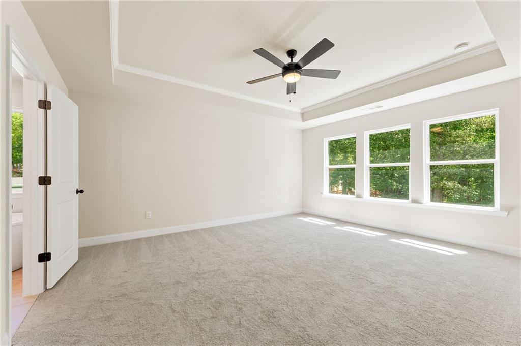 Spacious empty bedroom with large windows, ceiling fan, and neutral carpet in Davidson Homes The Hickory E, Buford, Georgia