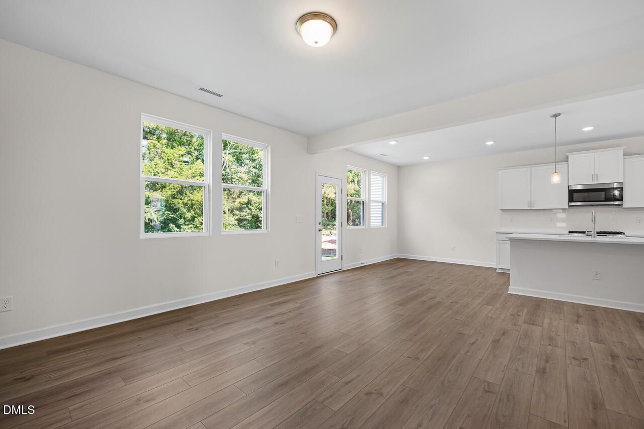 Bright open-concept living area with luxury vinyl plank flooring and white kitchen in The Willow B, Woodland Crossing, Zebulon NC