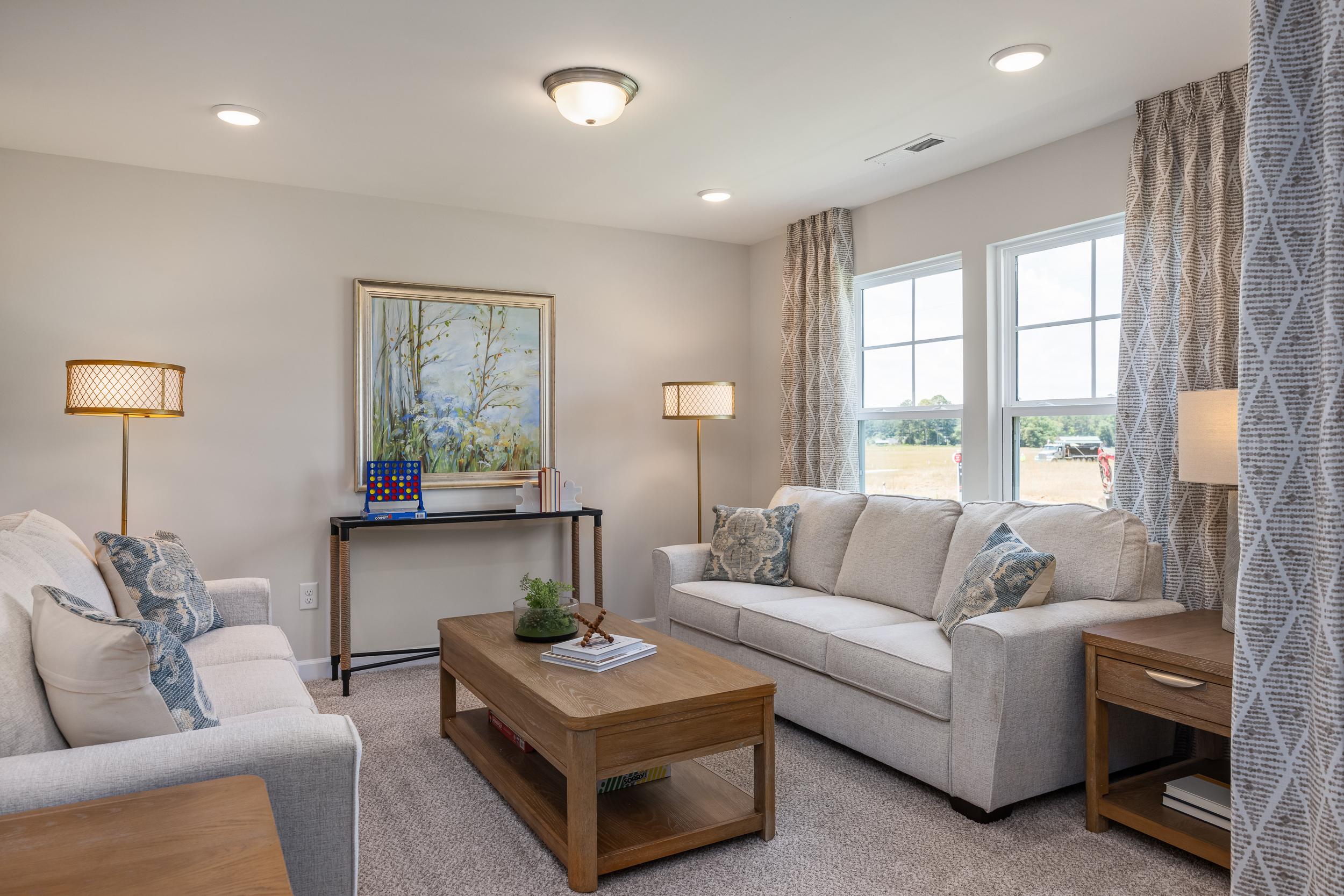 Cozy living room at Retreat at North Main in Lillington NC with beige sofas, wooden coffee table, lamps, and large windows