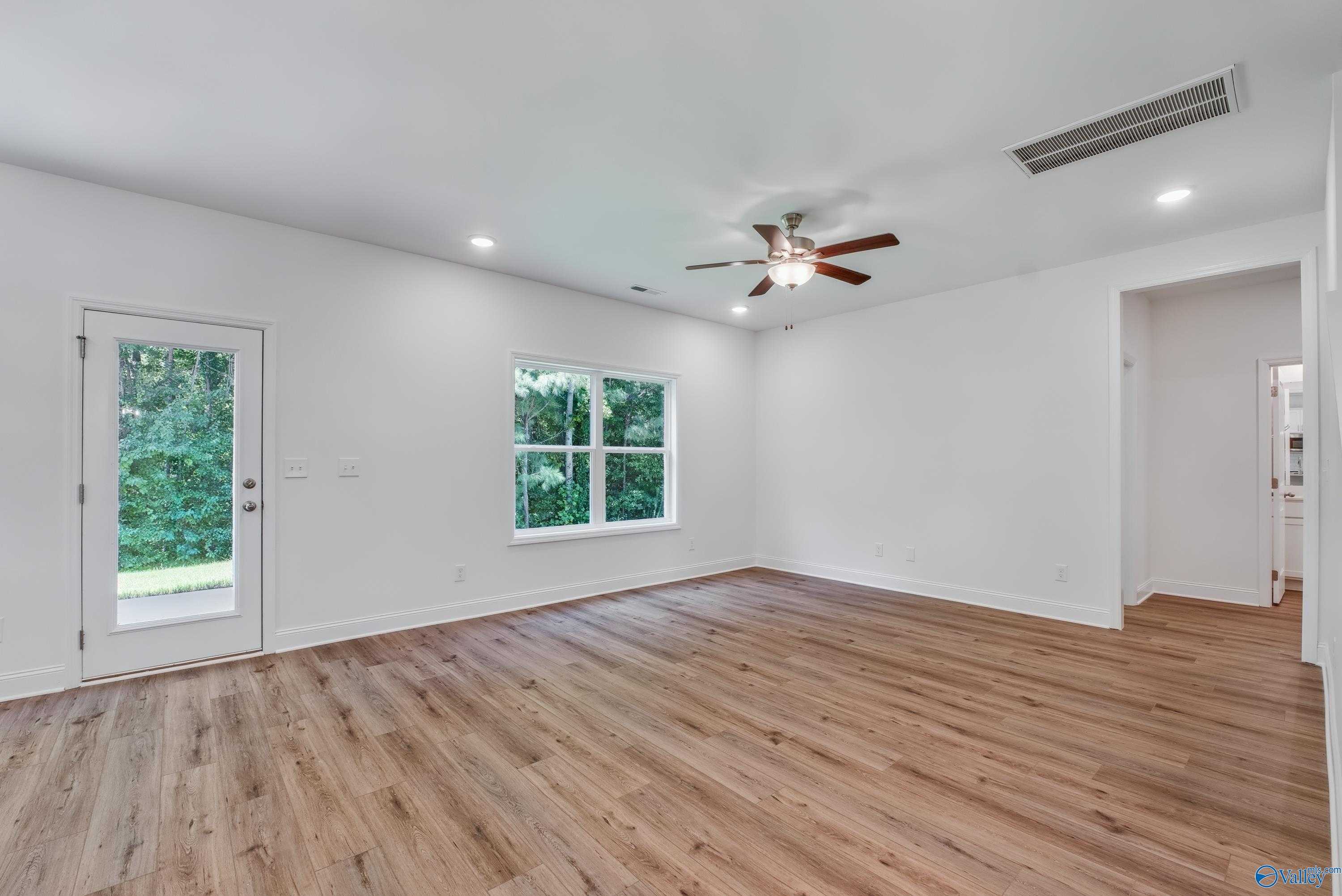 Bright family room with ceiling fan, large windows, and sliding glass door to lush backyard in The Shelby A, Davidson Homes, Arab, Alabama