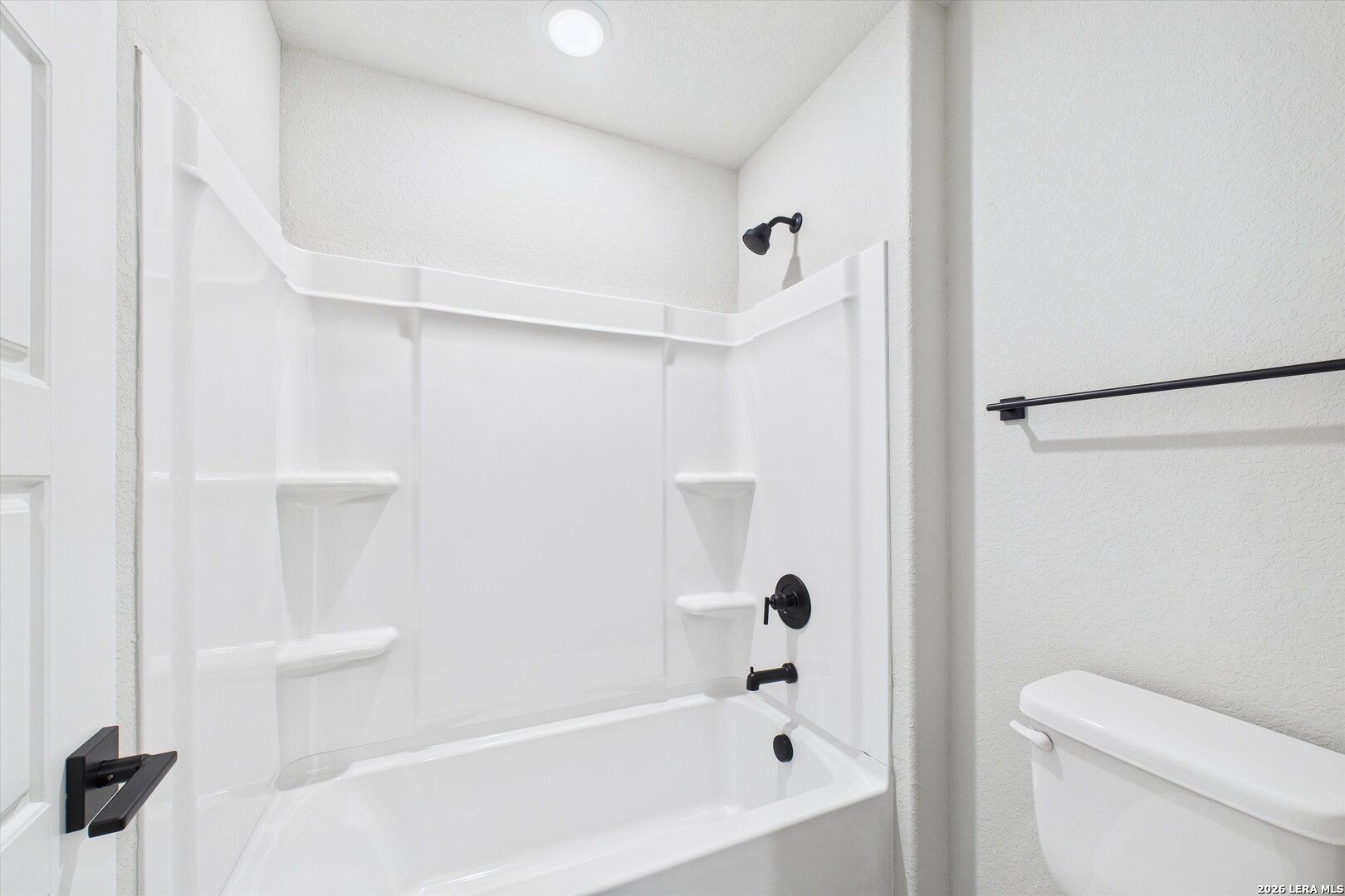 Bright modern bathroom with white tub-shower combo, glass enclosure, black fixtures in Davidson Homes The Charlotte A, San Antonio