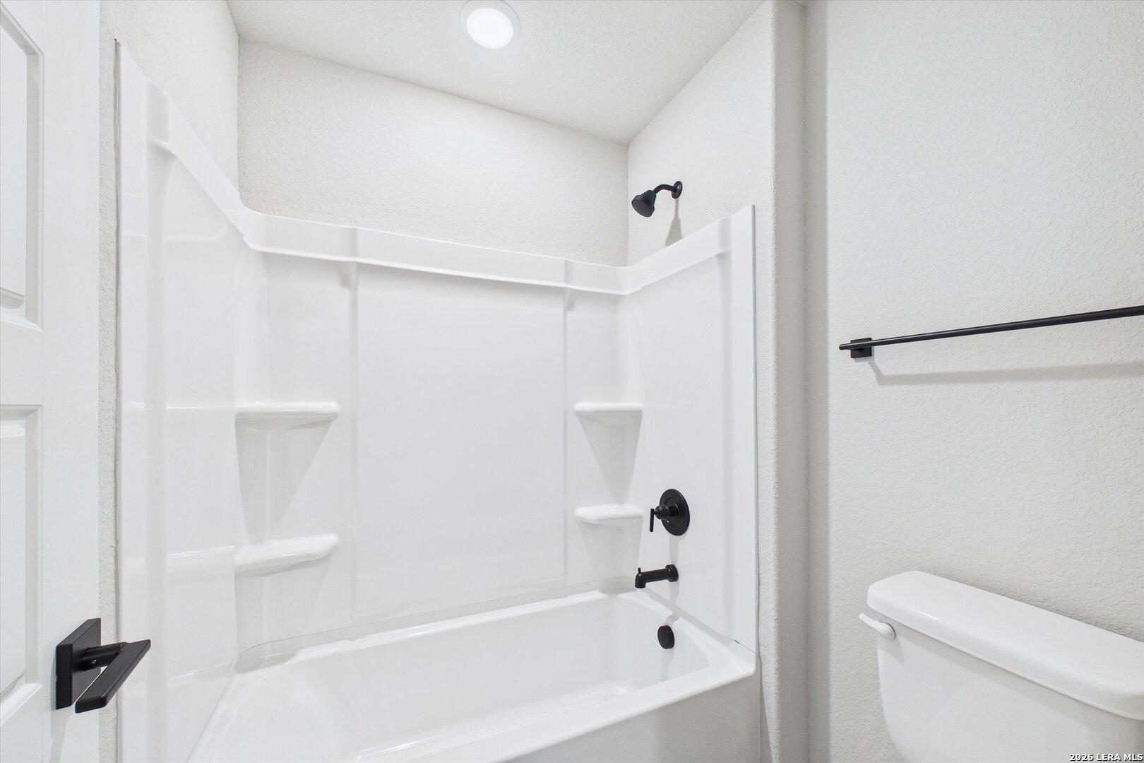 Bright modern bathroom with white tub-shower combo, glass enclosure, black fixtures in Davidson Homes The Charlotte A, San Antonio